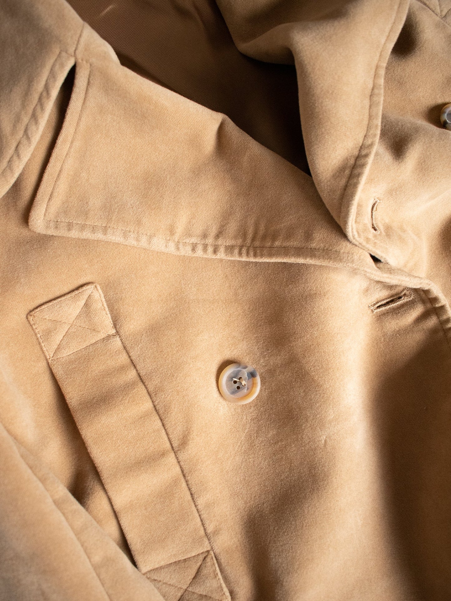 Close-up of a beige fabric with a button, possibly from a coat or jacket.