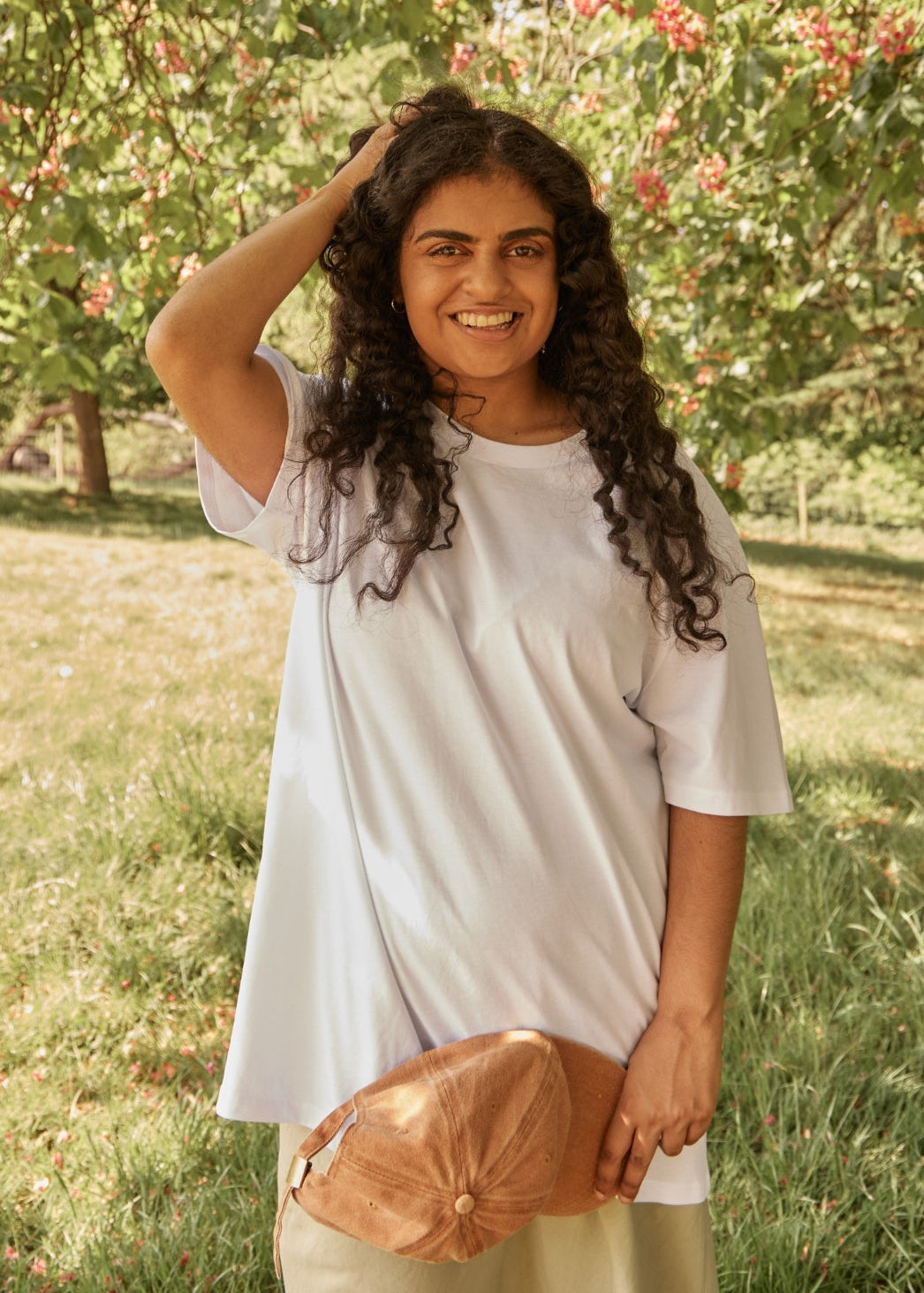 Woman standing in a grassy area with trees and flowers in the background