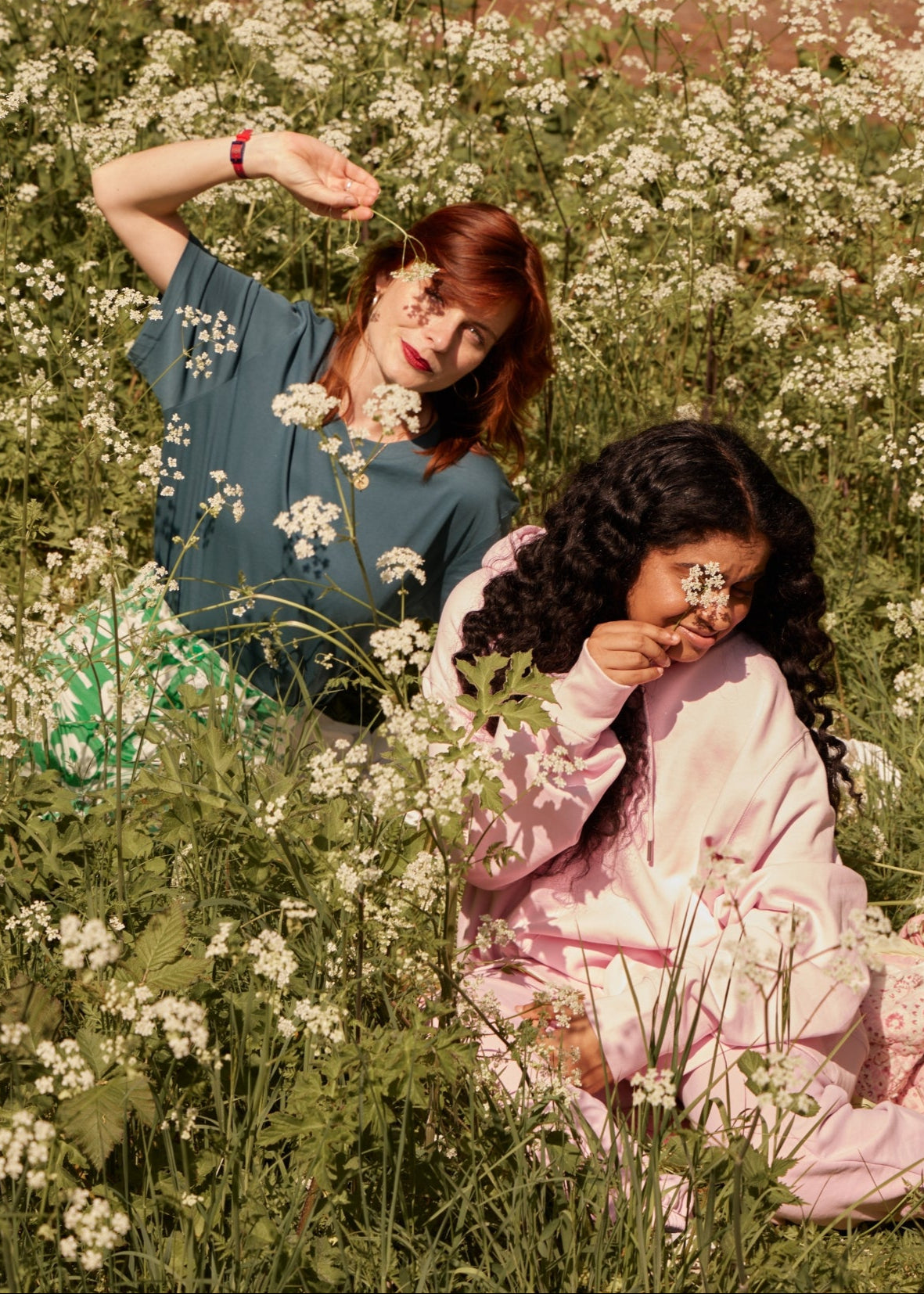 Two women sitting in a field of white flowers, surrounded by greenery.