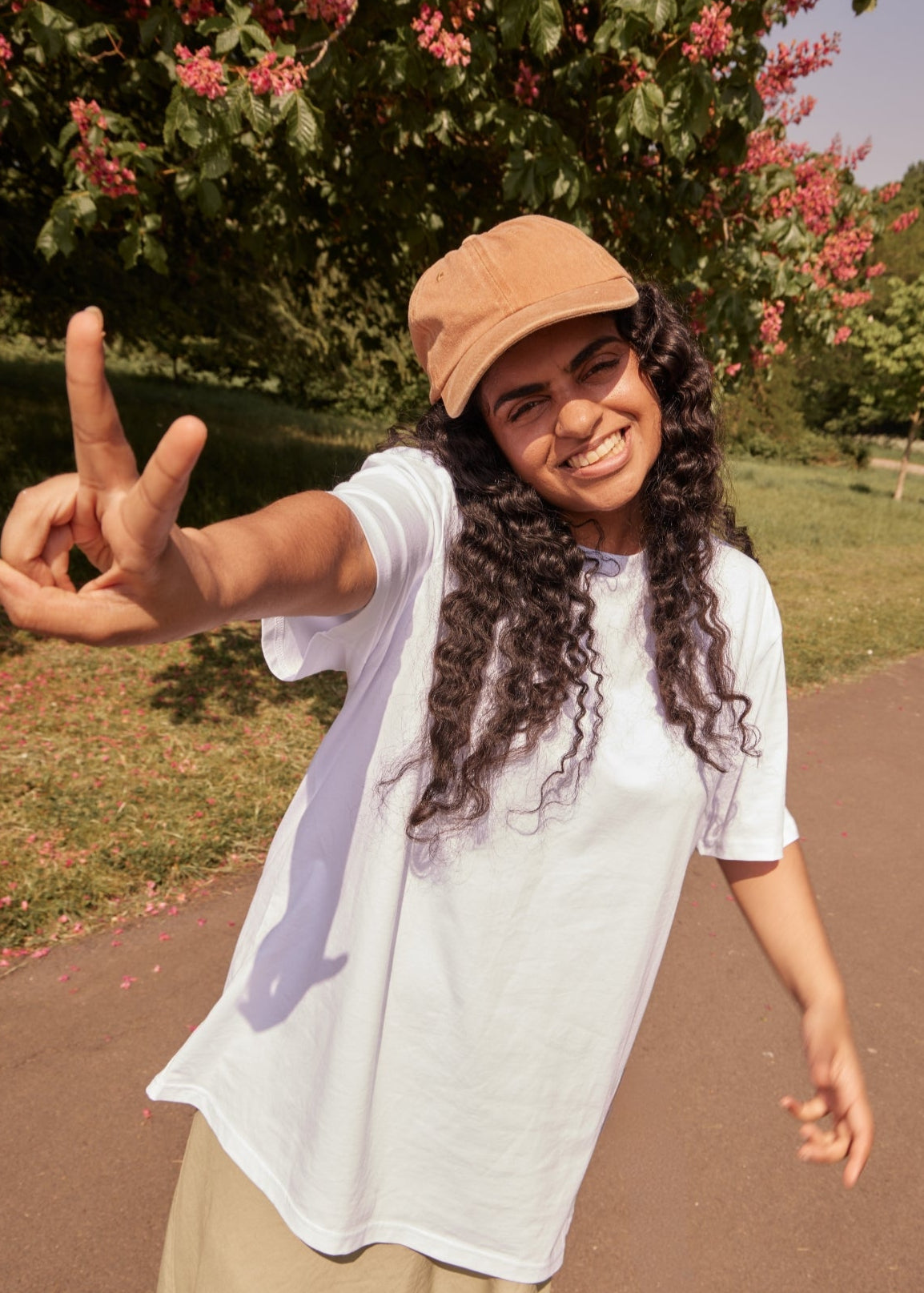 Person wearing a beige cap and white shirt, making a peace sign outdoors.