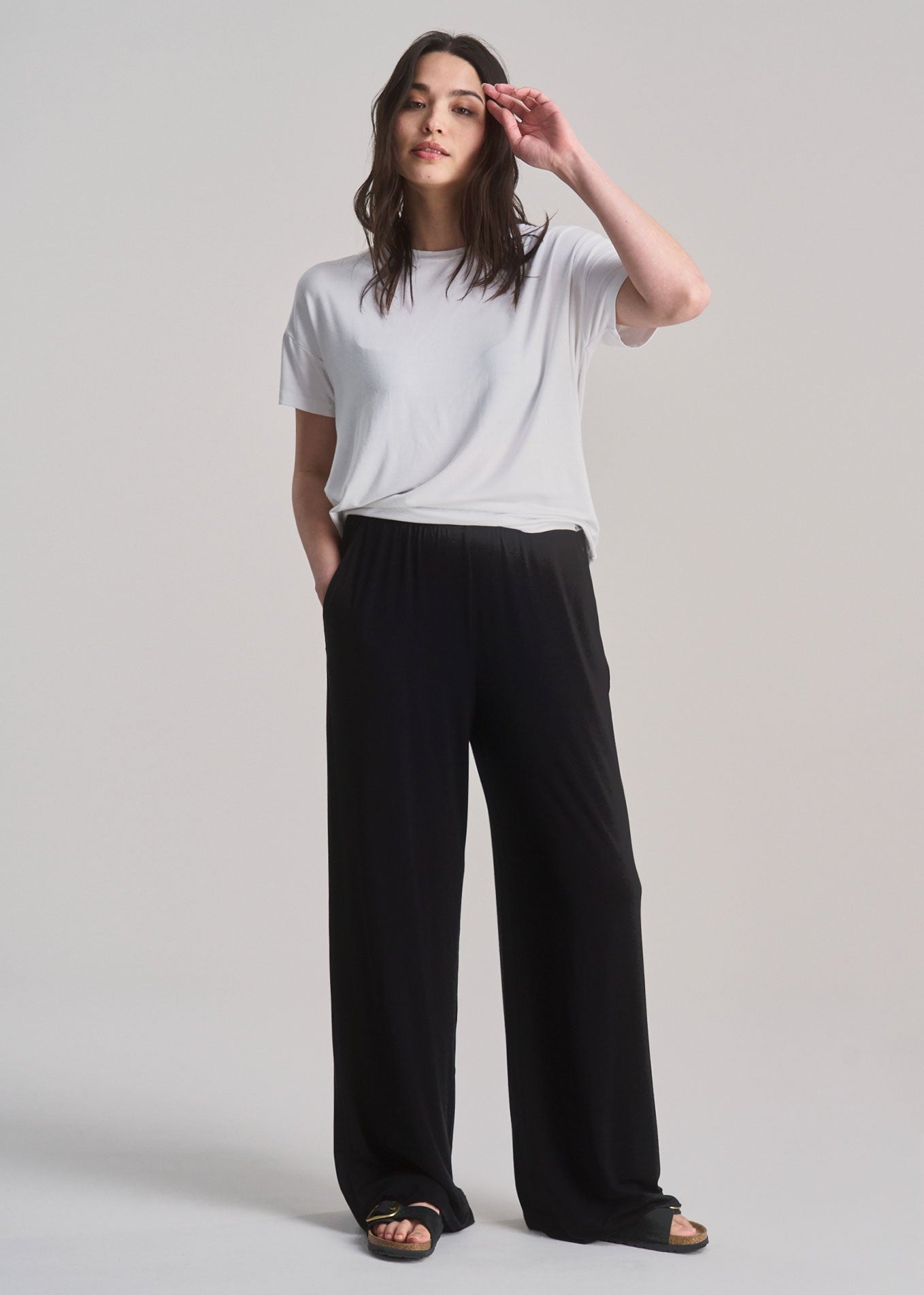 Woman wearing a white t-shirt and black pants on a light gray background