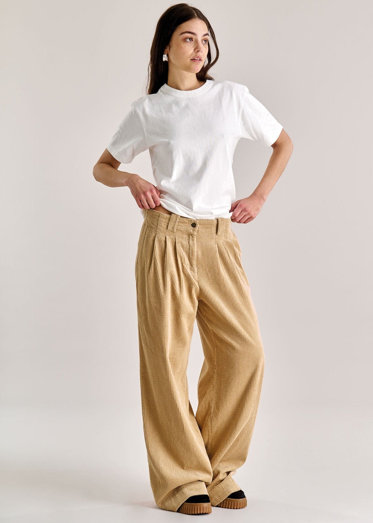 Person wearing a white shirt and beige wide-leg pants on a plain background