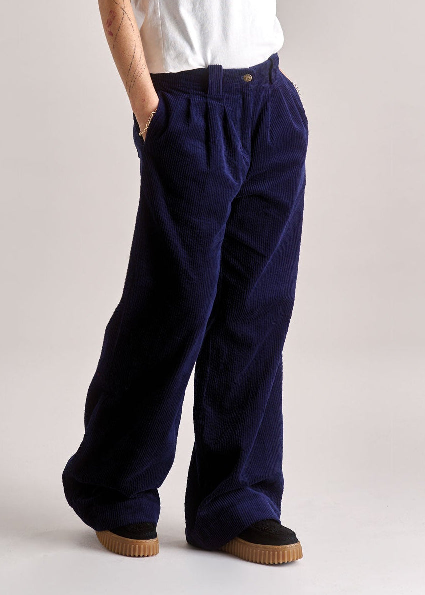 Woman wearing a white shirt and navy pants on a plain background
