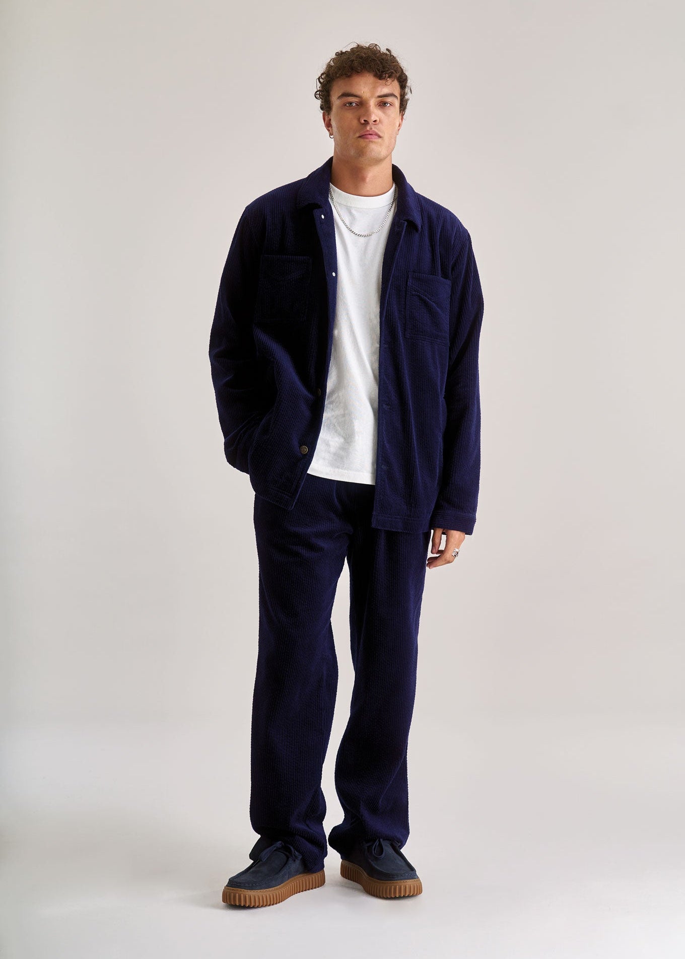 Man wearing a navy jacket, white shirt, and dark pants on a plain background