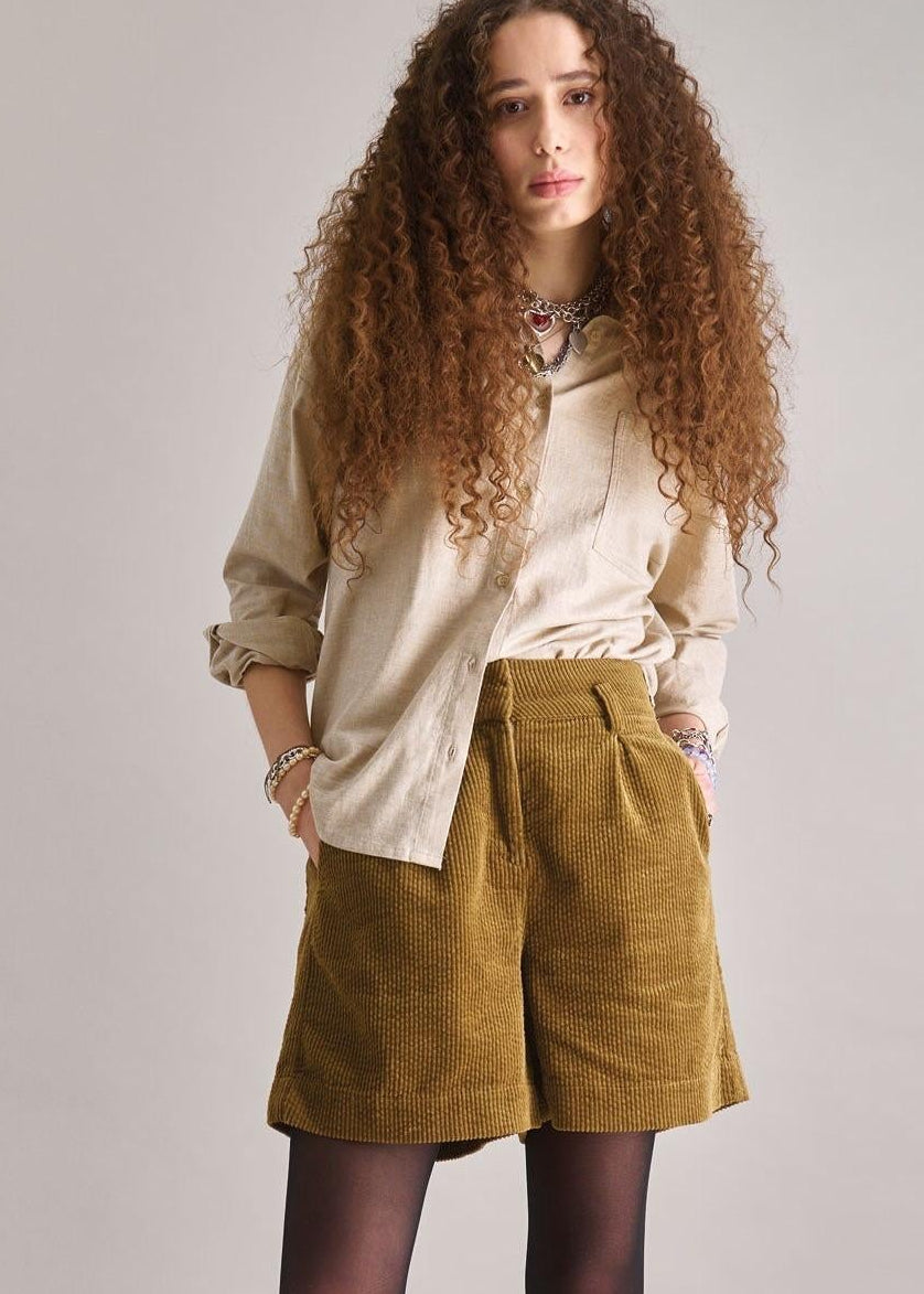 Woman wearing a beige shirt, brown shorts, and black shoes on a plain background