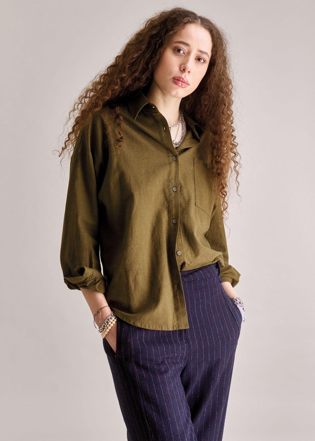 Woman wearing an olive green shirt and purple pants against a plain background