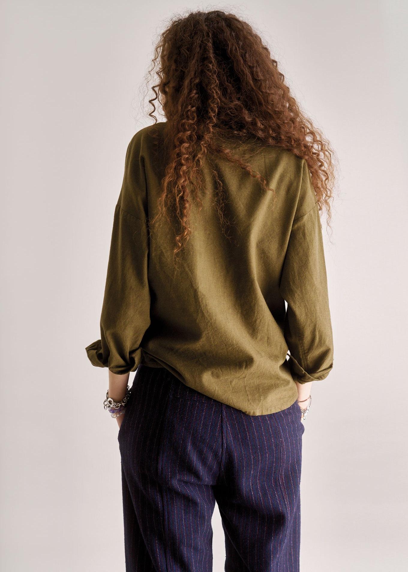 Person wearing a green shirt and dark pants with long curly hair on a plain background