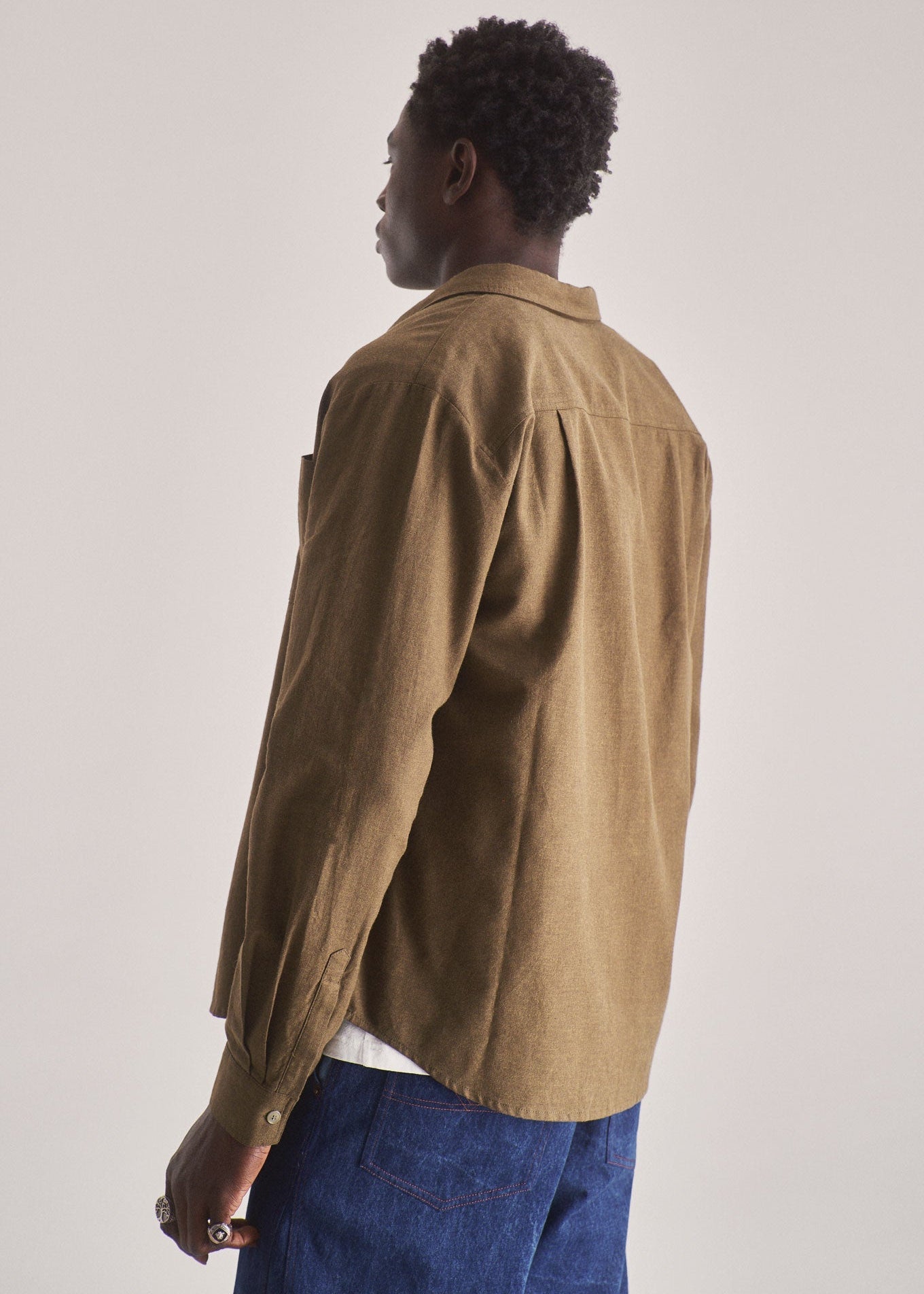 Person wearing a brown jacket and blue pants against a plain background