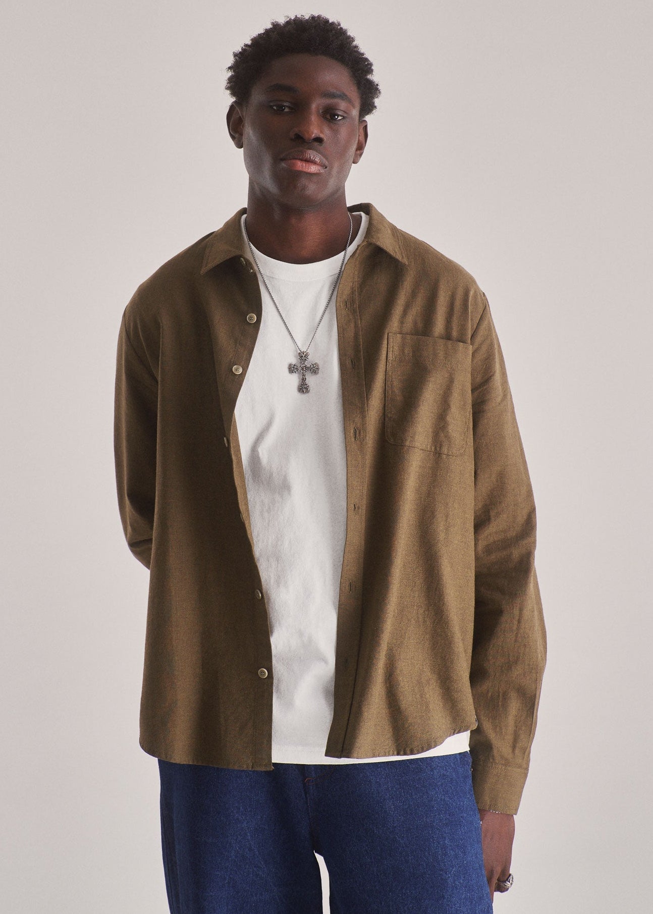 Man wearing a brown corduroy shirt over a white t-shirt with blue pants on a plain background