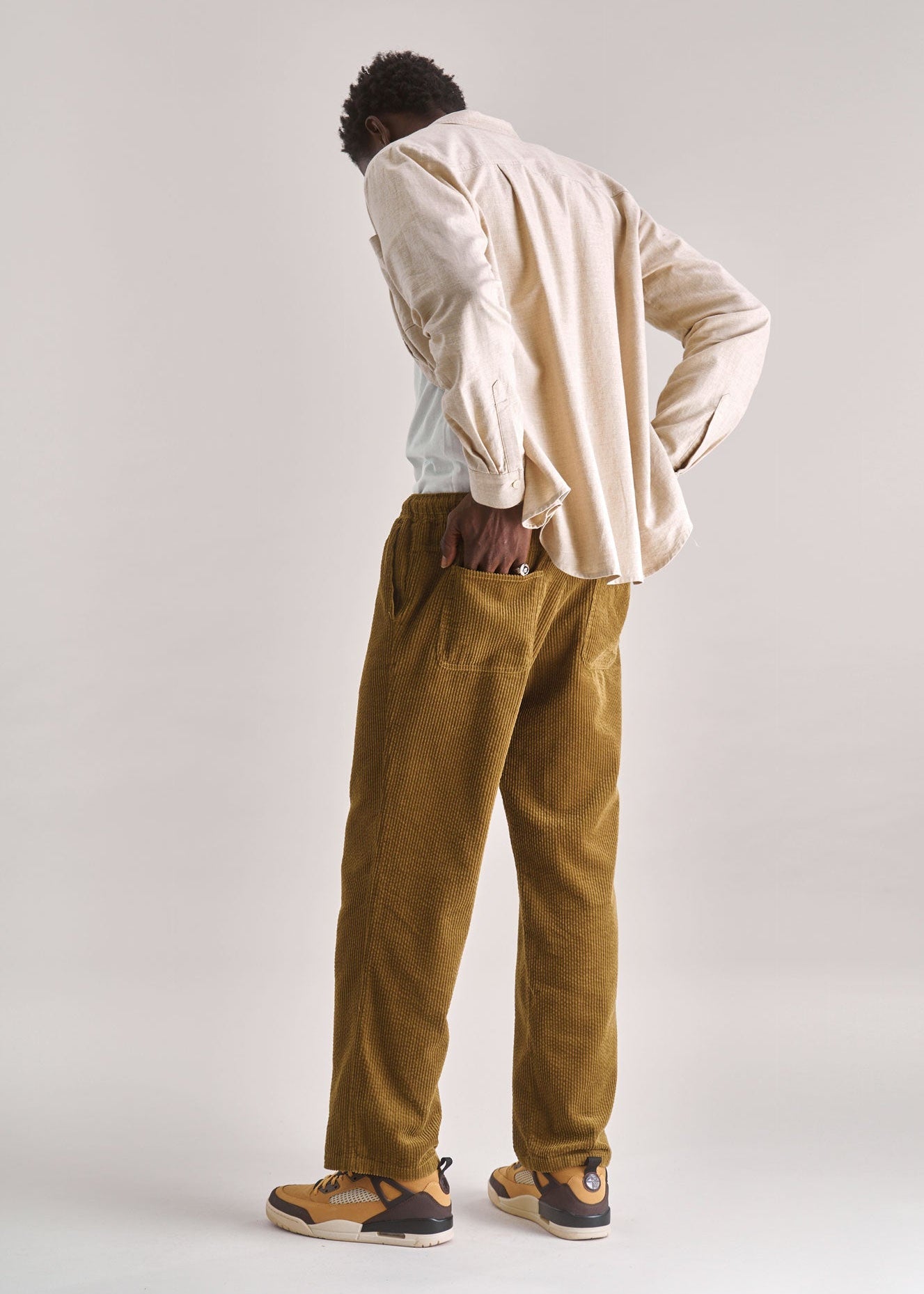 Person wearing a beige shirt and mustard yellow pants on a plain background