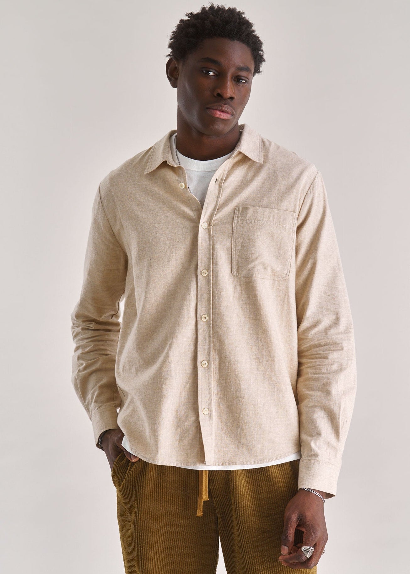 Man wearing a beige shirt and mustard pants against a white background