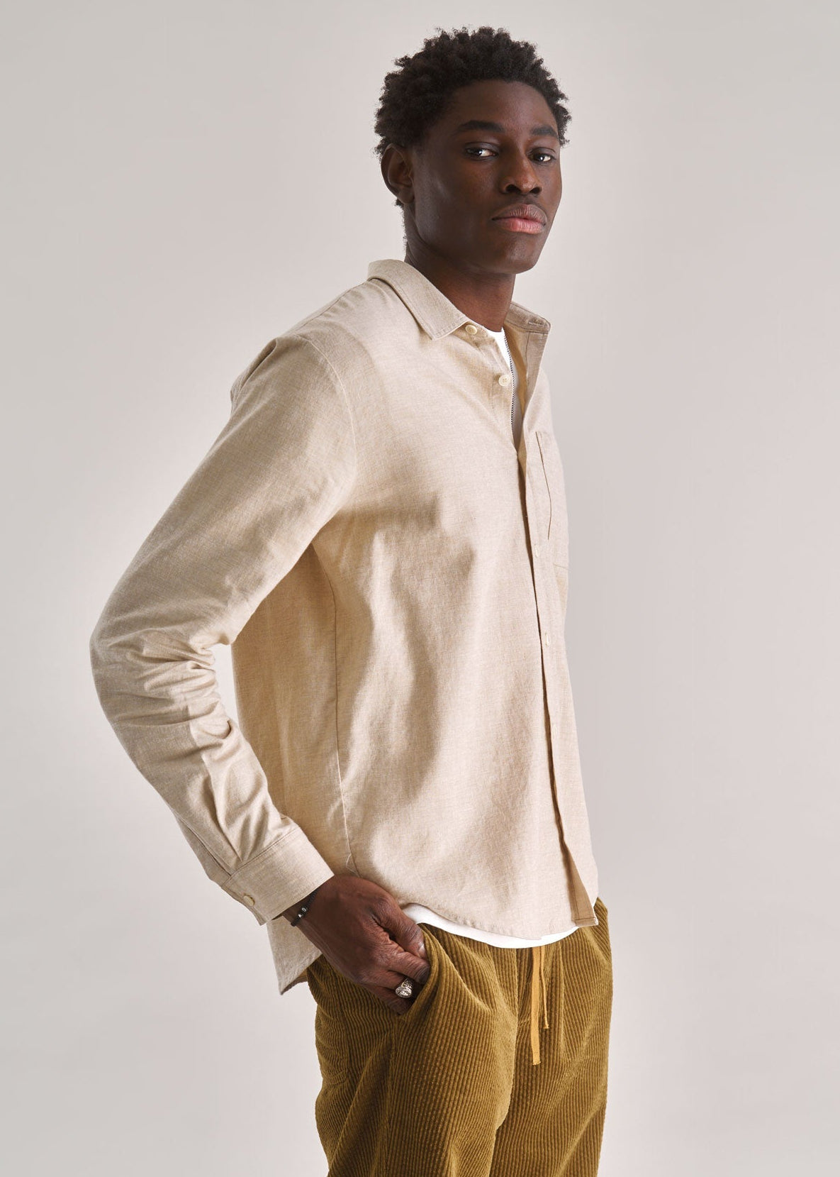 Man wearing a beige shirt and mustard pants against a white background