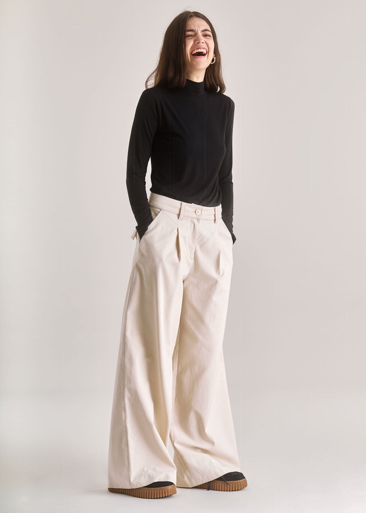 Person wearing a black long-sleeve top and beige wide-leg pants on a white background