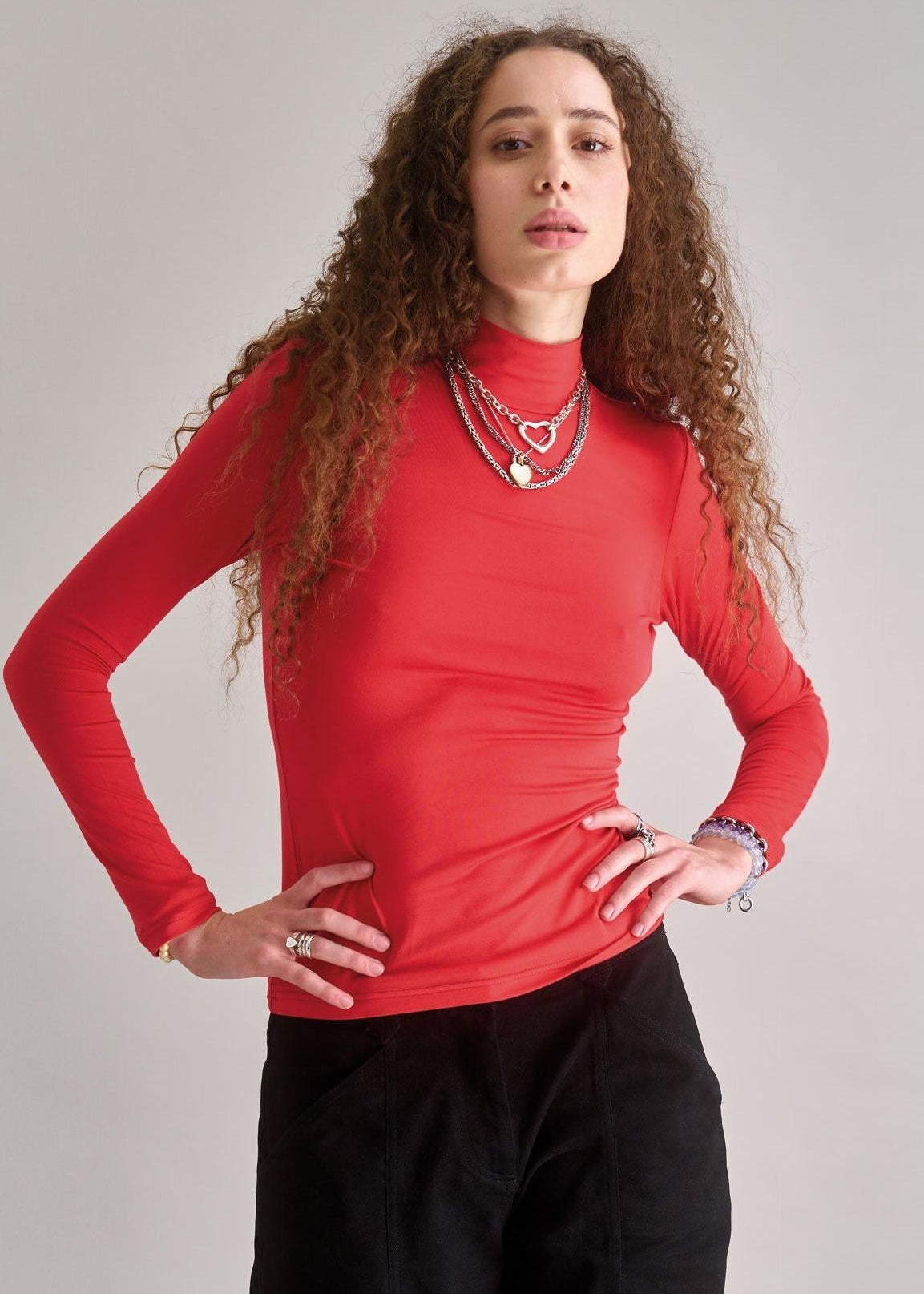 Person wearing a red long-sleeve top and black pants against a plain background