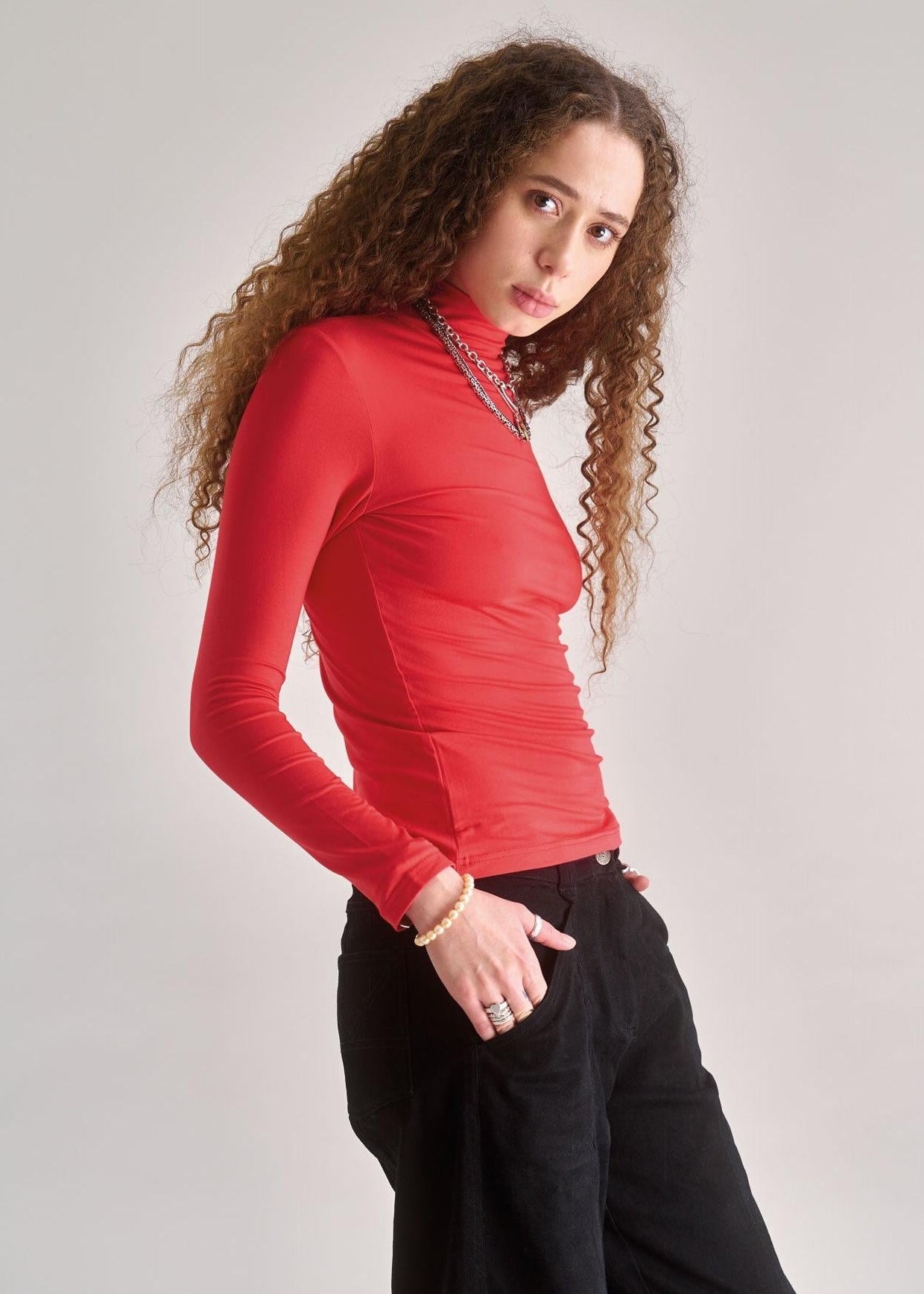 Woman wearing a red long-sleeve top and black pants against a plain background