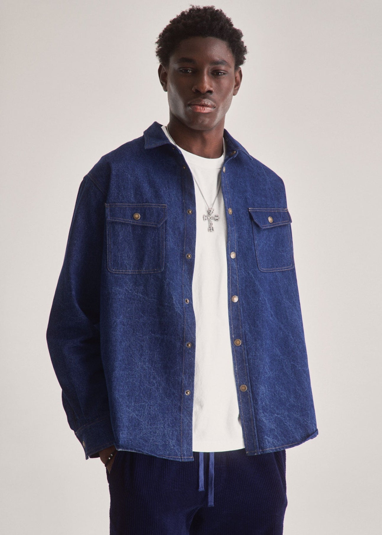 Man wearing a blue denim jacket over a white shirt on a plain background