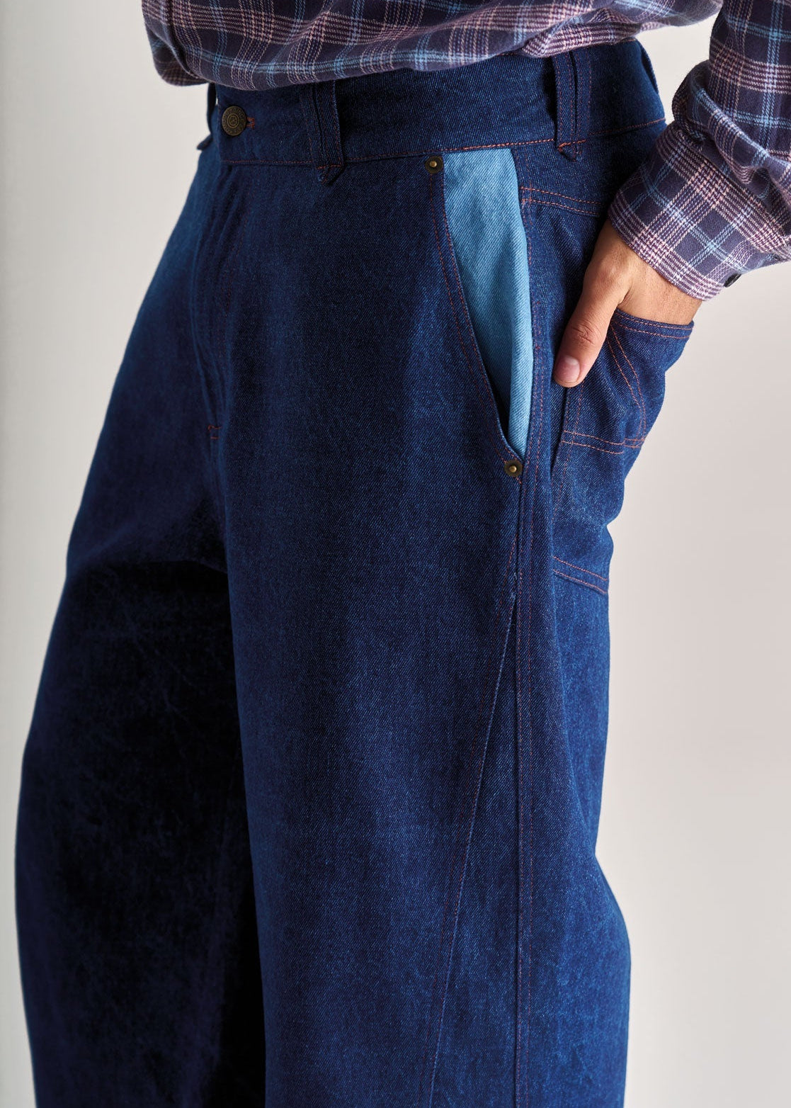 Person wearing a plaid shirt and blue denim pants on a plain background