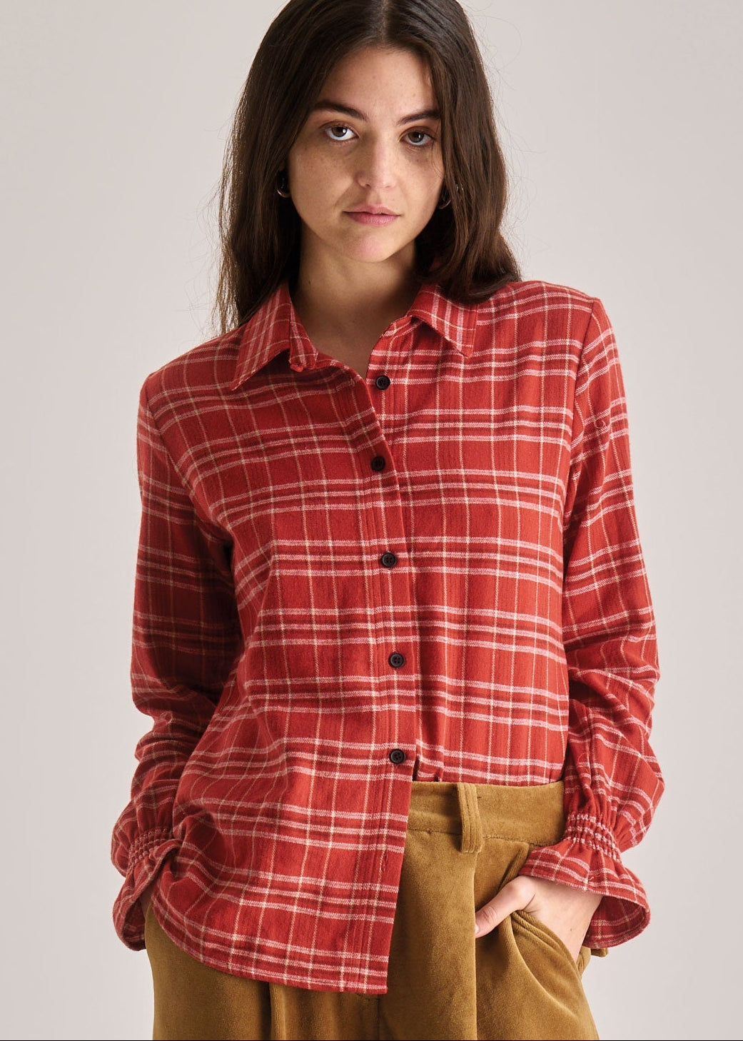 Woman wearing a red plaid shirt and brown pants against a plain background