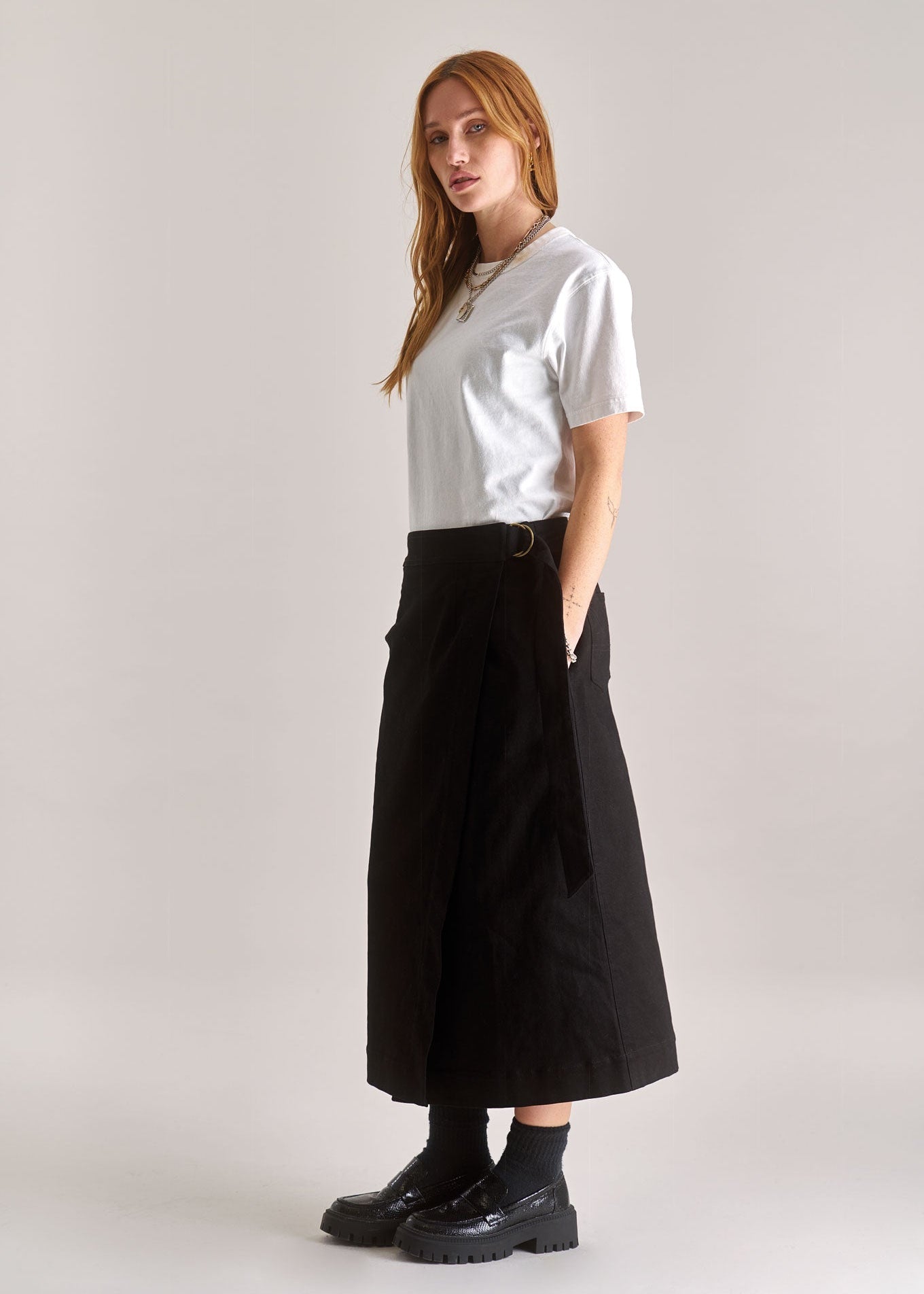Person wearing a white t-shirt, black skirt, and black shoes on a plain background