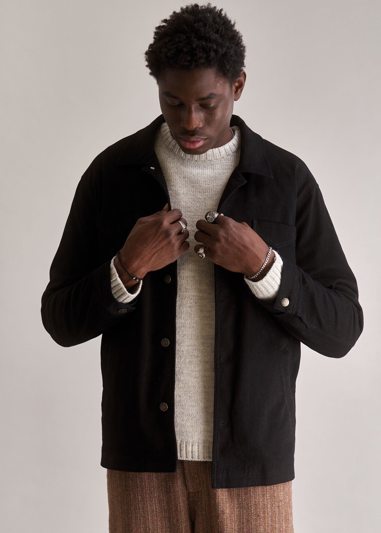 Man wearing a black jacket over a white sweater on a plain background
