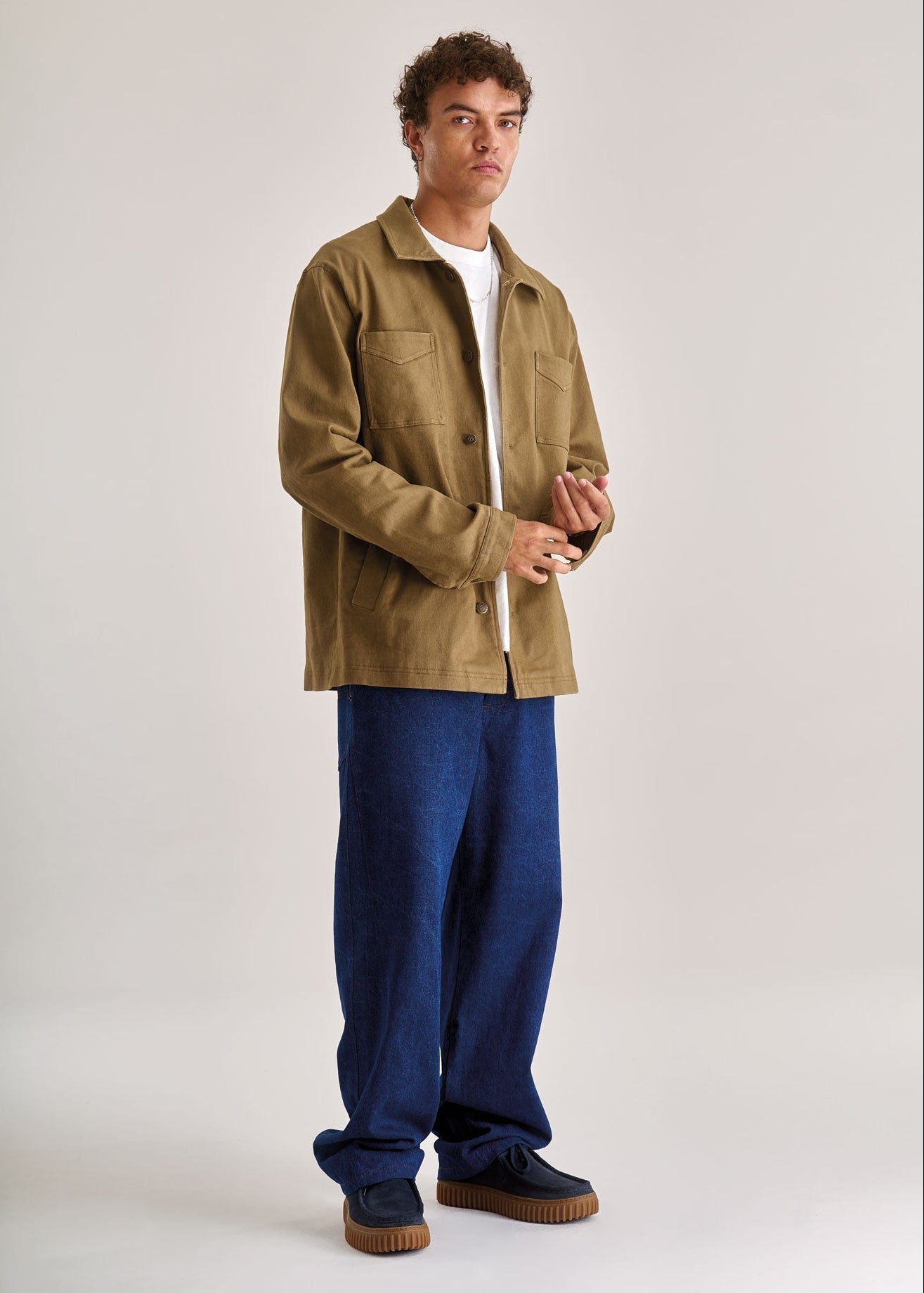 Man wearing a brown jacket and blue pants on a white background