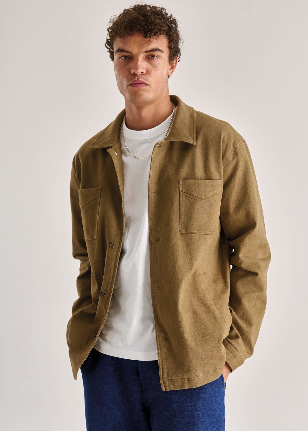 Man wearing a brown jacket over a white shirt and blue pants on a white background