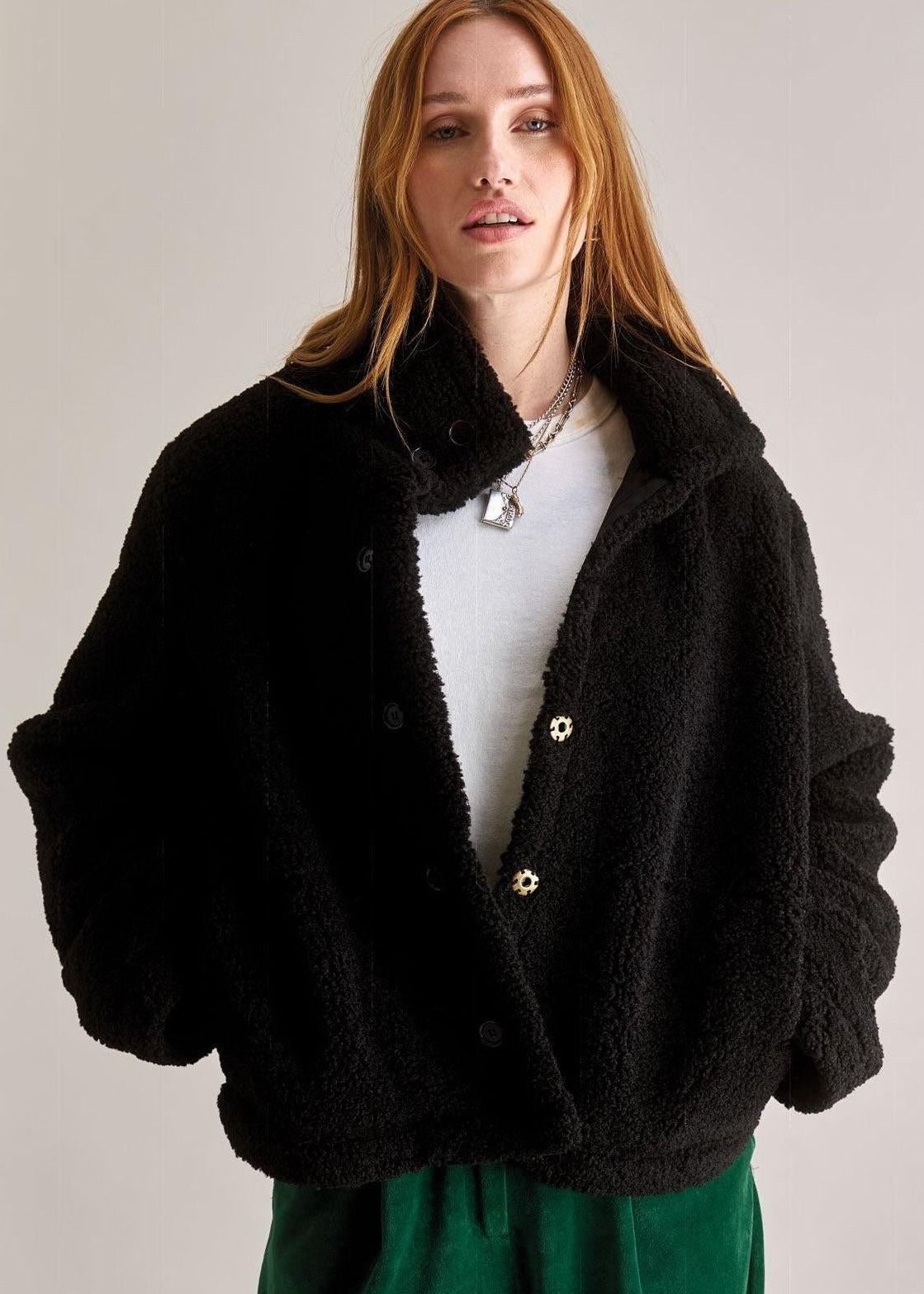 Woman wearing a black jacket and green pants against a plain background