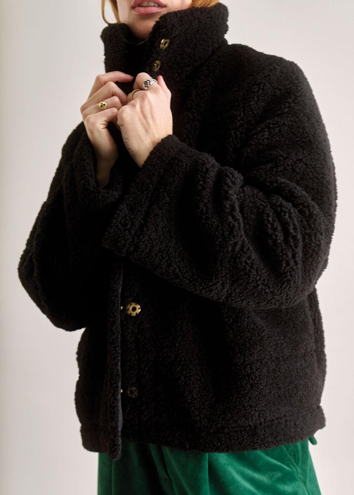 Person wearing a black textured jacket with green pants on a plain background