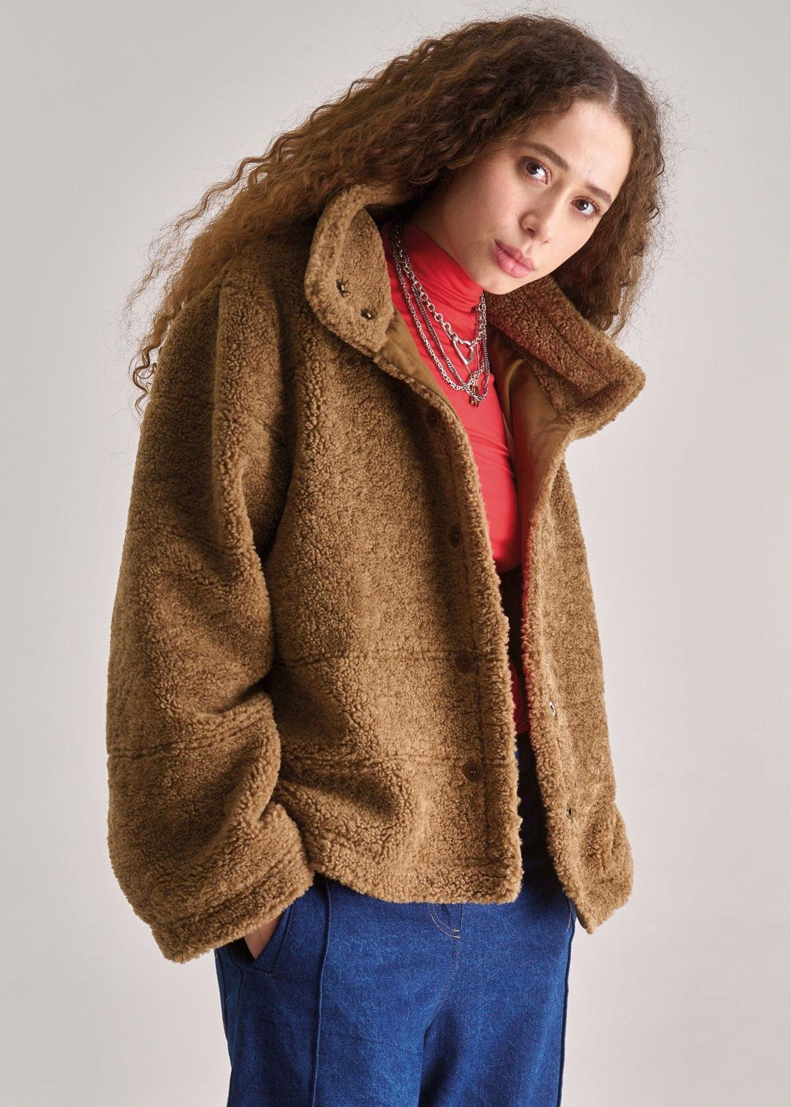 Woman wearing a brown jacket over a red top with a white background