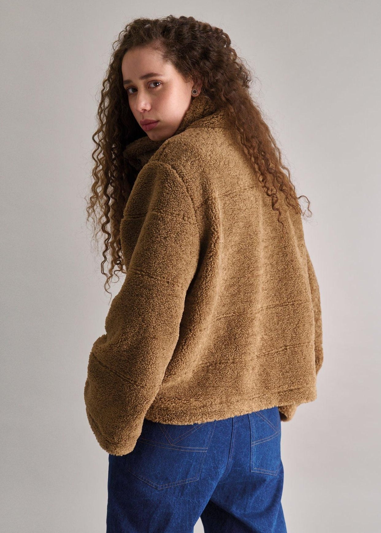 Person wearing a brown fuzzy jacket and blue pants against a plain background