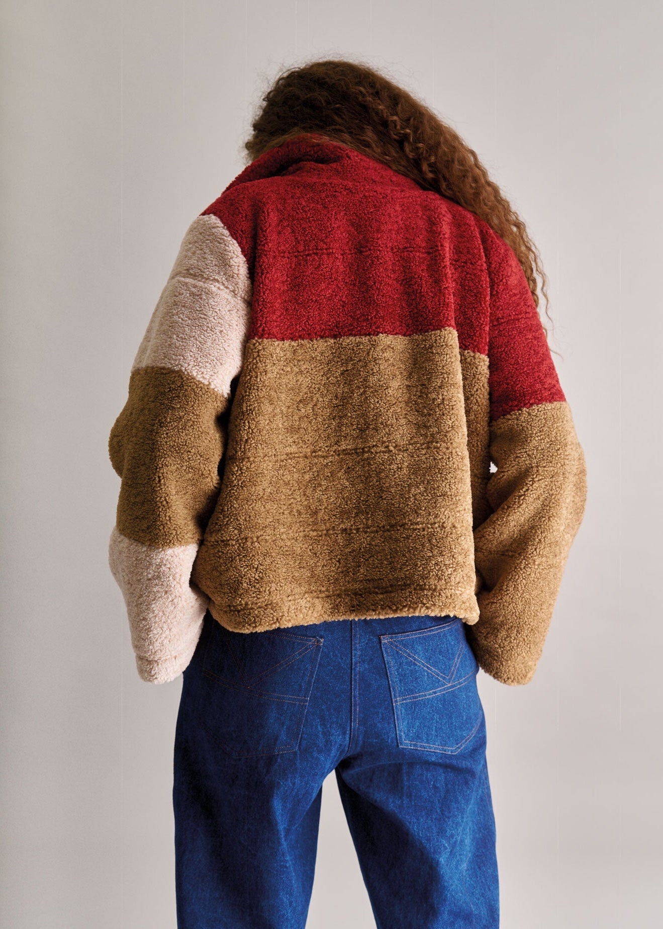 Person wearing a color-blocked sweater with red, beige, and white sections on a plain background