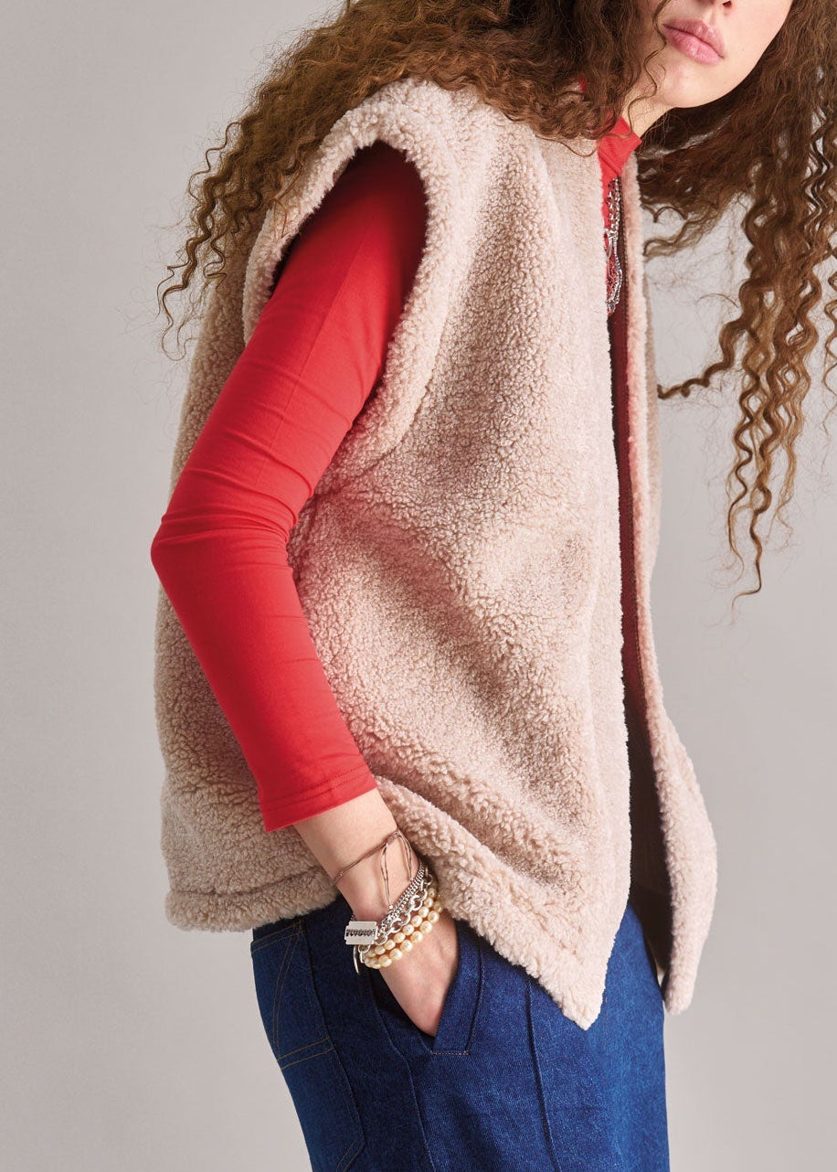 Person wearing a beige fleece vest over a red shirt with a neutral background