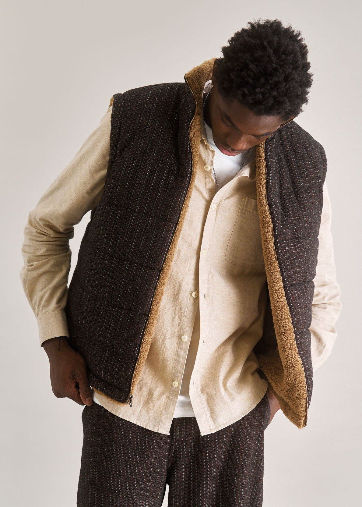 Person wearing a brown vest over a beige shirt with a plain background