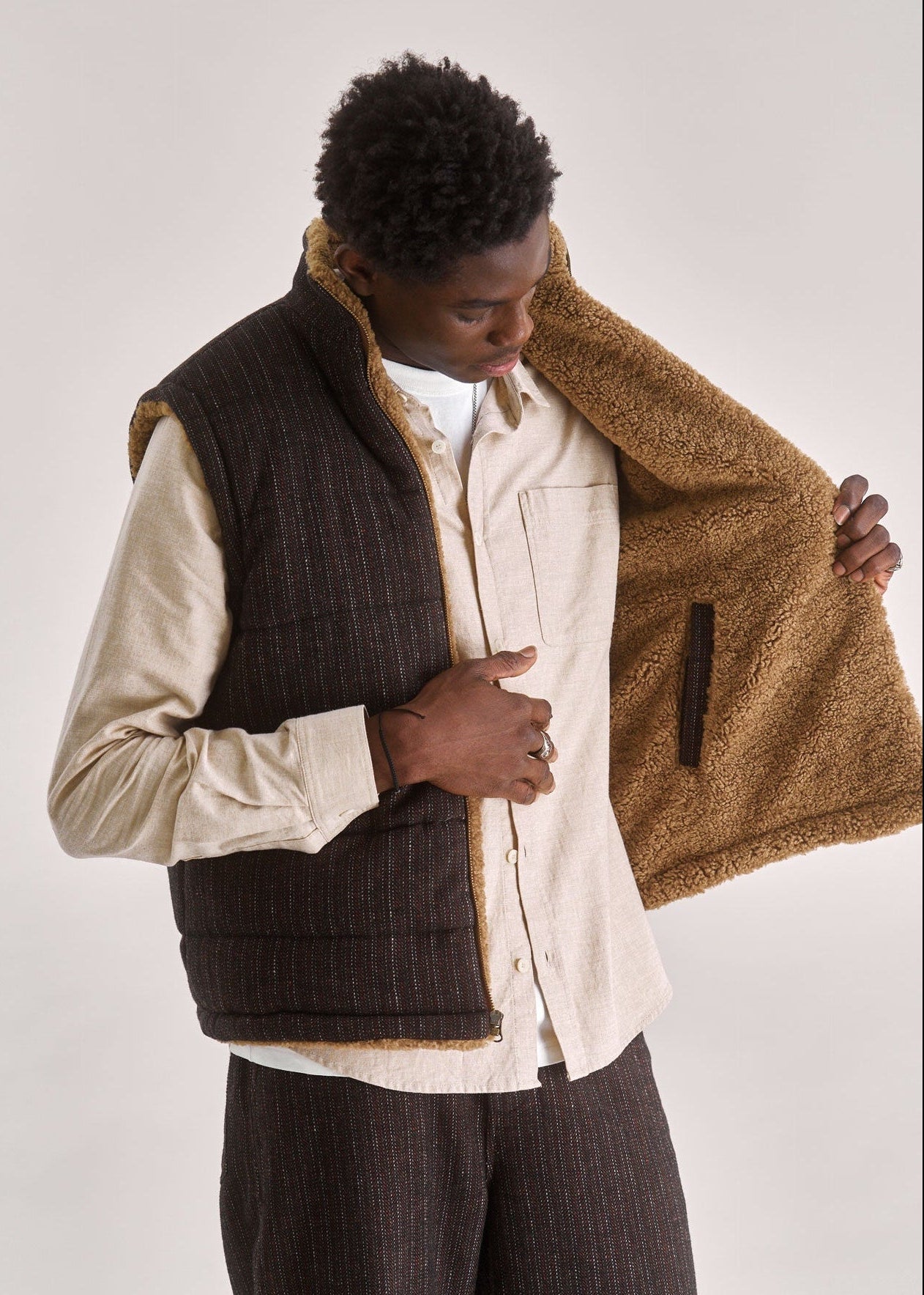 Person wearing a brown fleece vest over a beige shirt on a white background