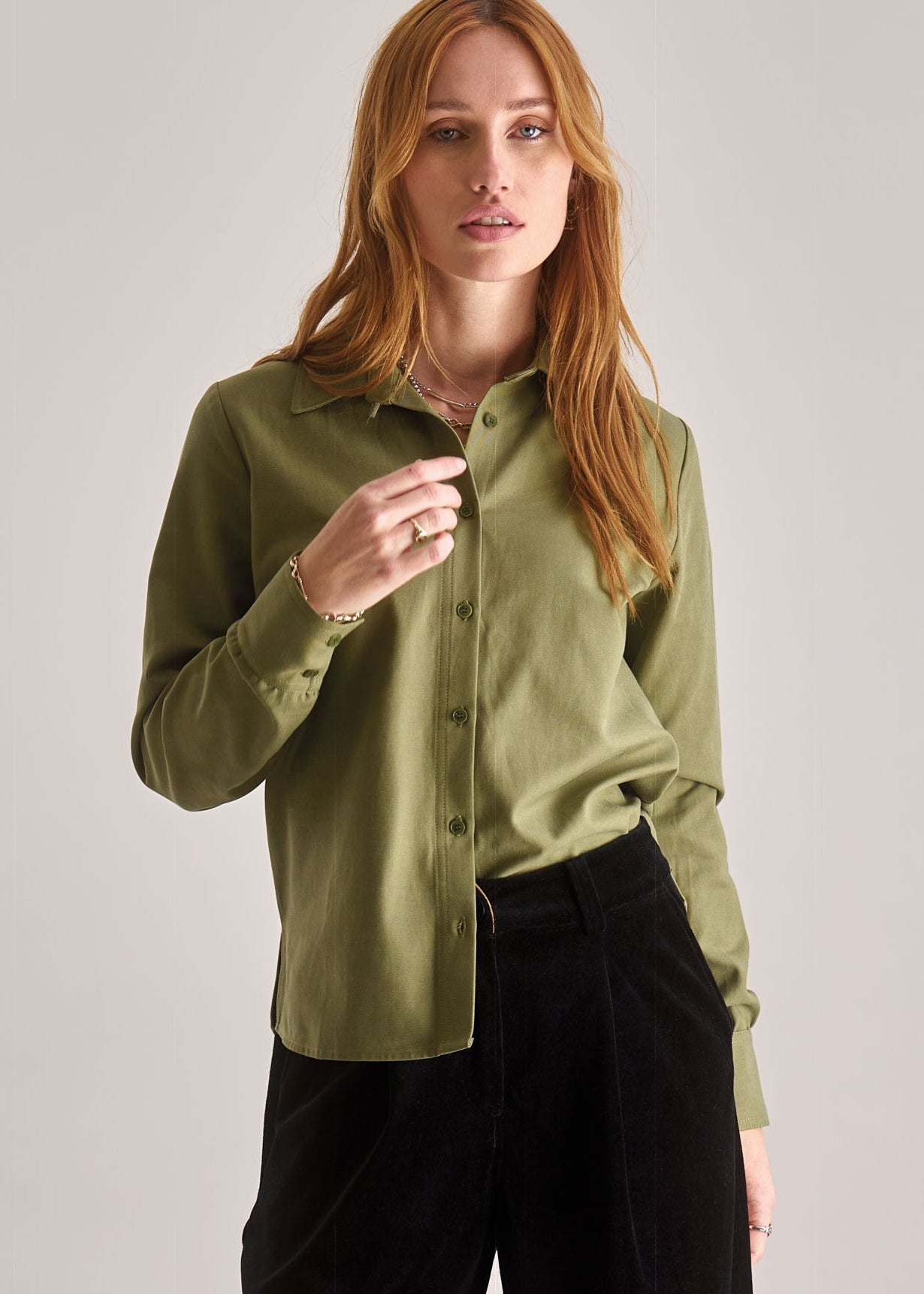 Woman wearing a green blouse and black pants against a plain background