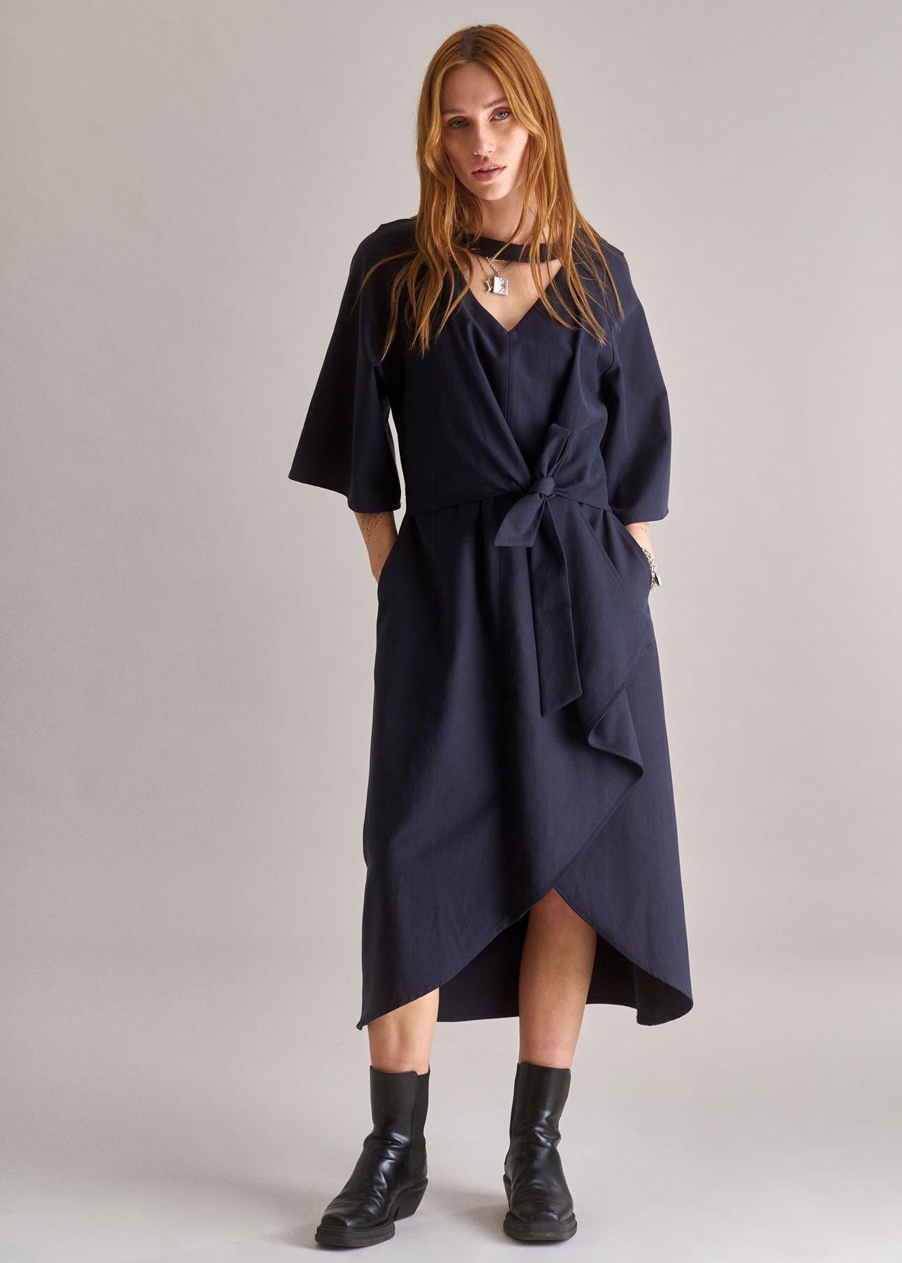 Woman wearing a navy blue dress with a belt on a plain background