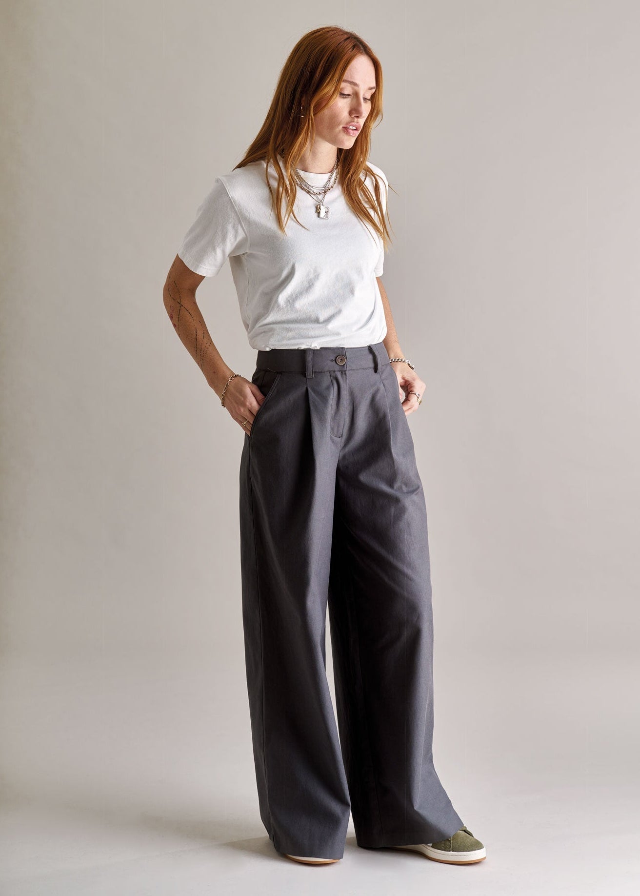 Woman wearing a white t-shirt and gray wide-leg pants against a plain background