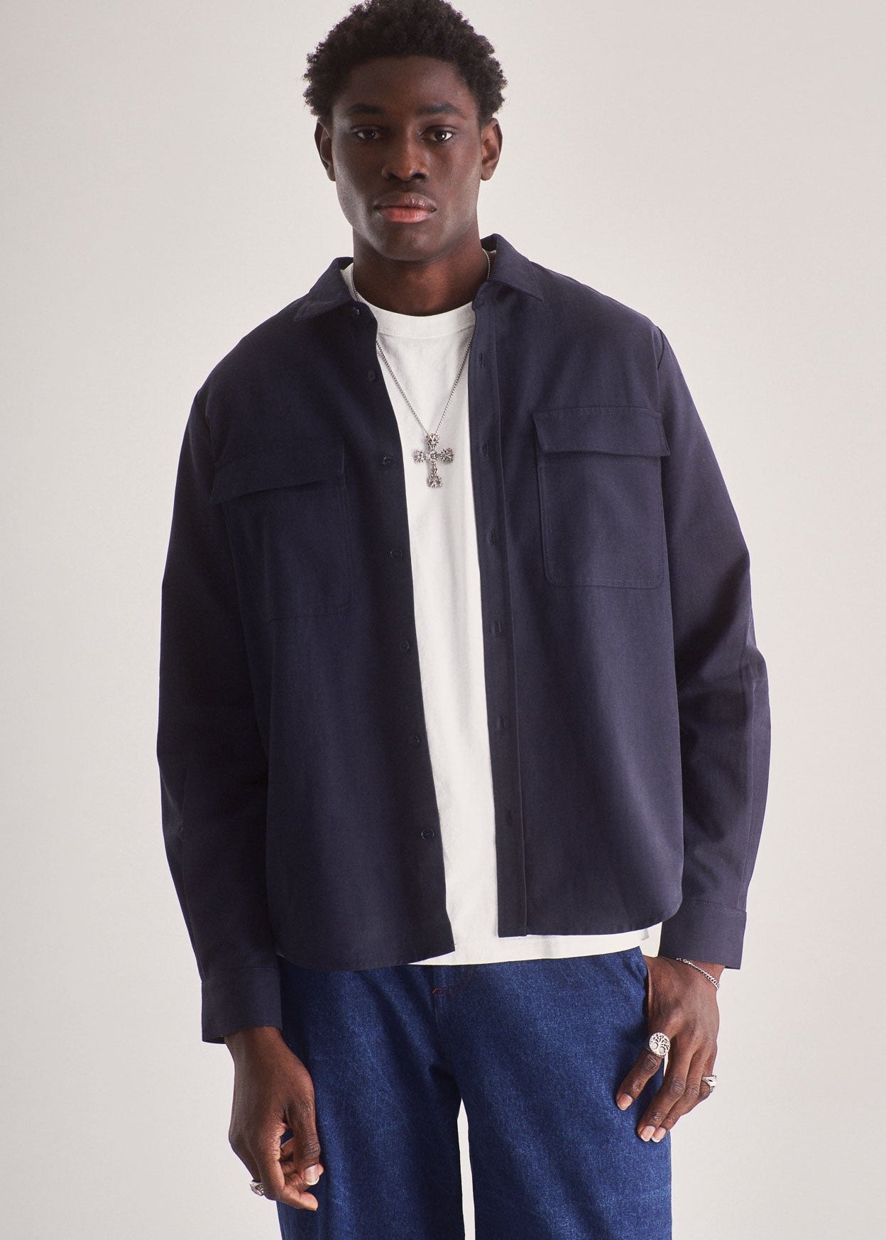 Man wearing a navy jacket over a white shirt with blue pants on a plain background