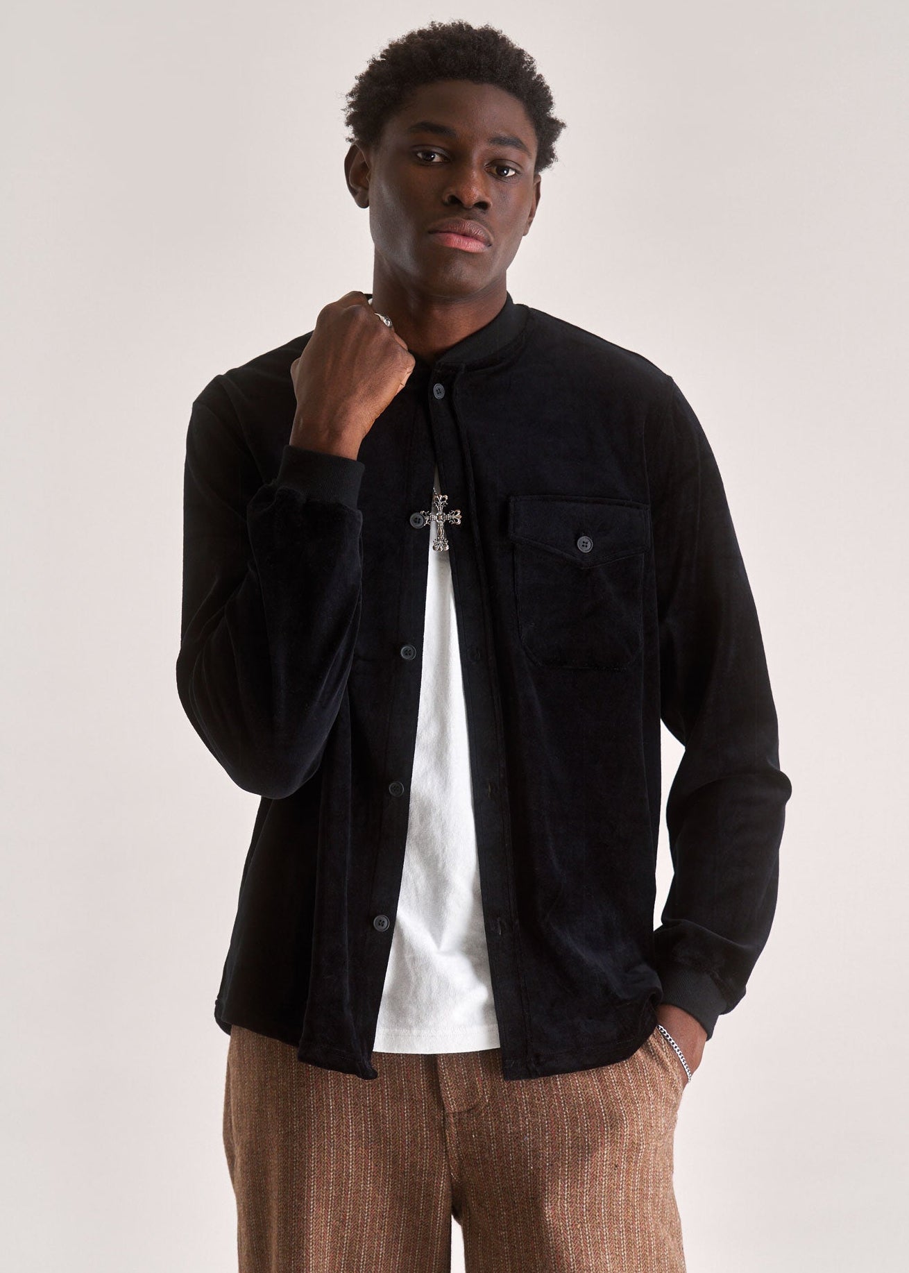 Man wearing a black shirt over a white t-shirt with brown pants on a plain background