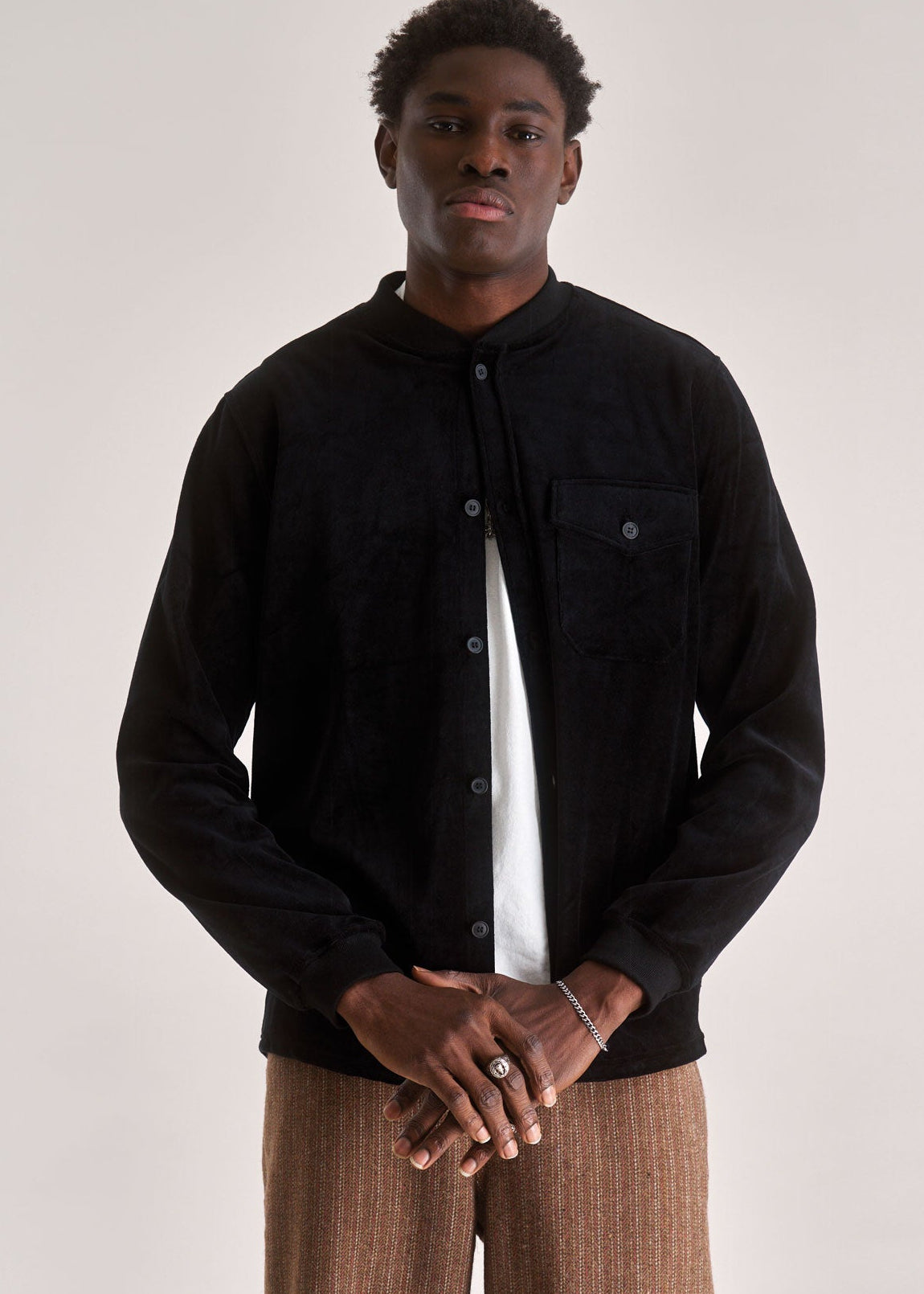 Man wearing a black jacket and brown pants against a plain background