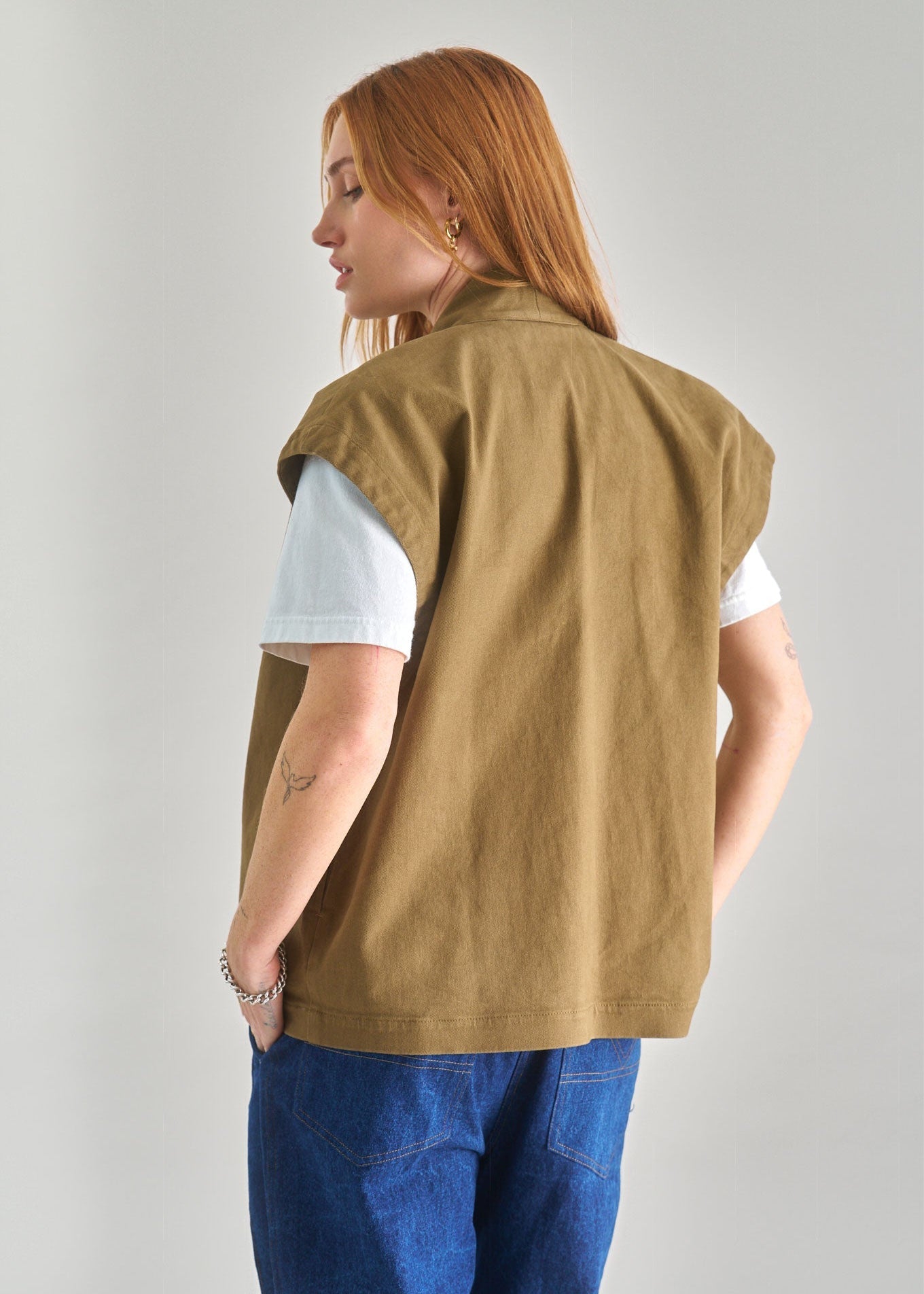 Person wearing a brown vest over a white shirt with blue pants on a plain background