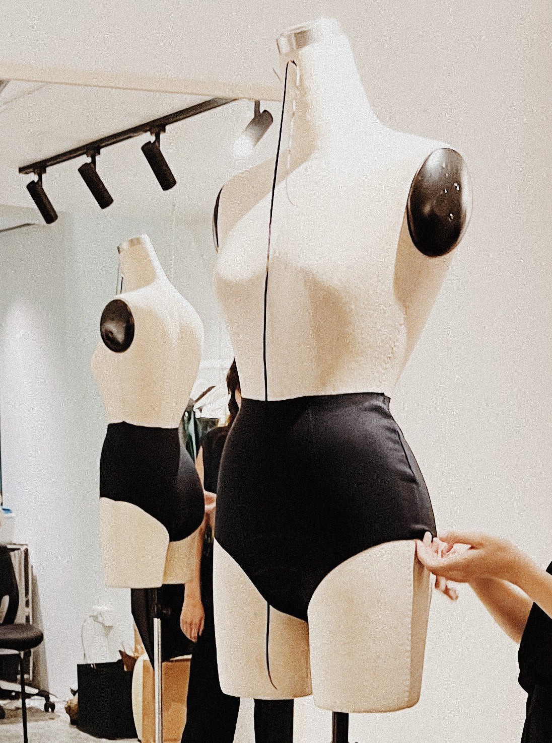 Mannequins with black outfits on display in a room with lighting fixtures.