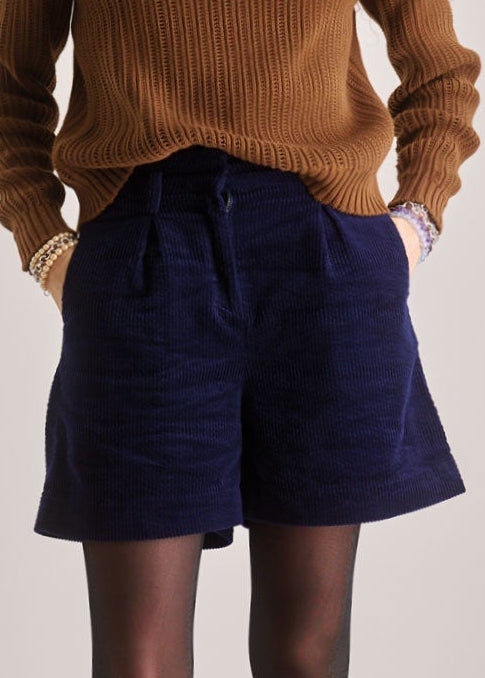 Woman wearing a brown sweater and purple shorts on a plain background