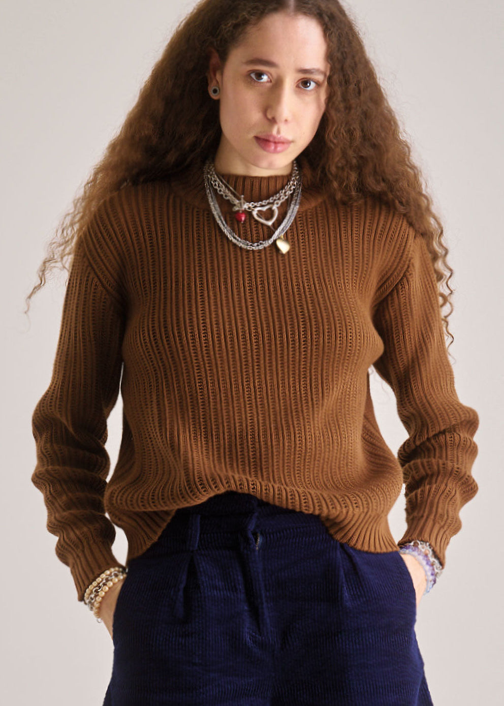 Woman wearing a brown sweater and blue pants against a plain background