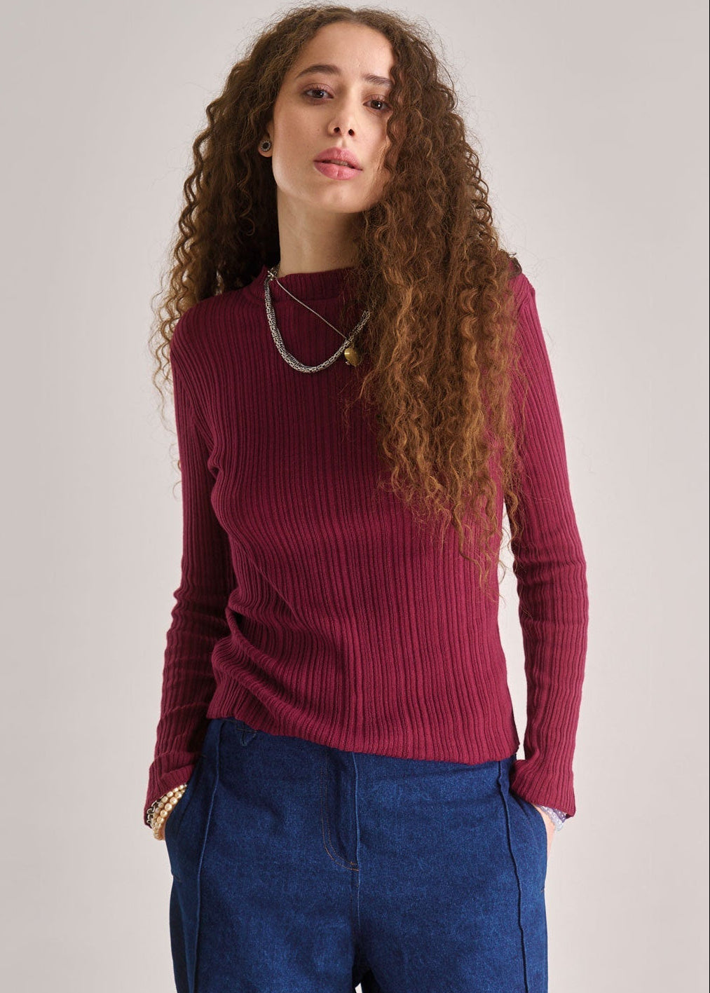 Woman wearing a burgundy ribbed sweater and blue pants against a plain background