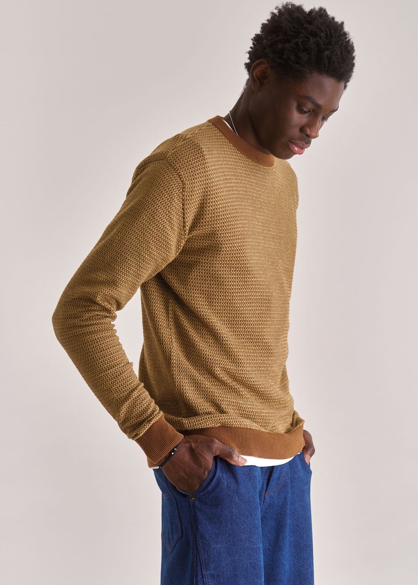 Man wearing a brown knitted sweater and blue pants against a plain background