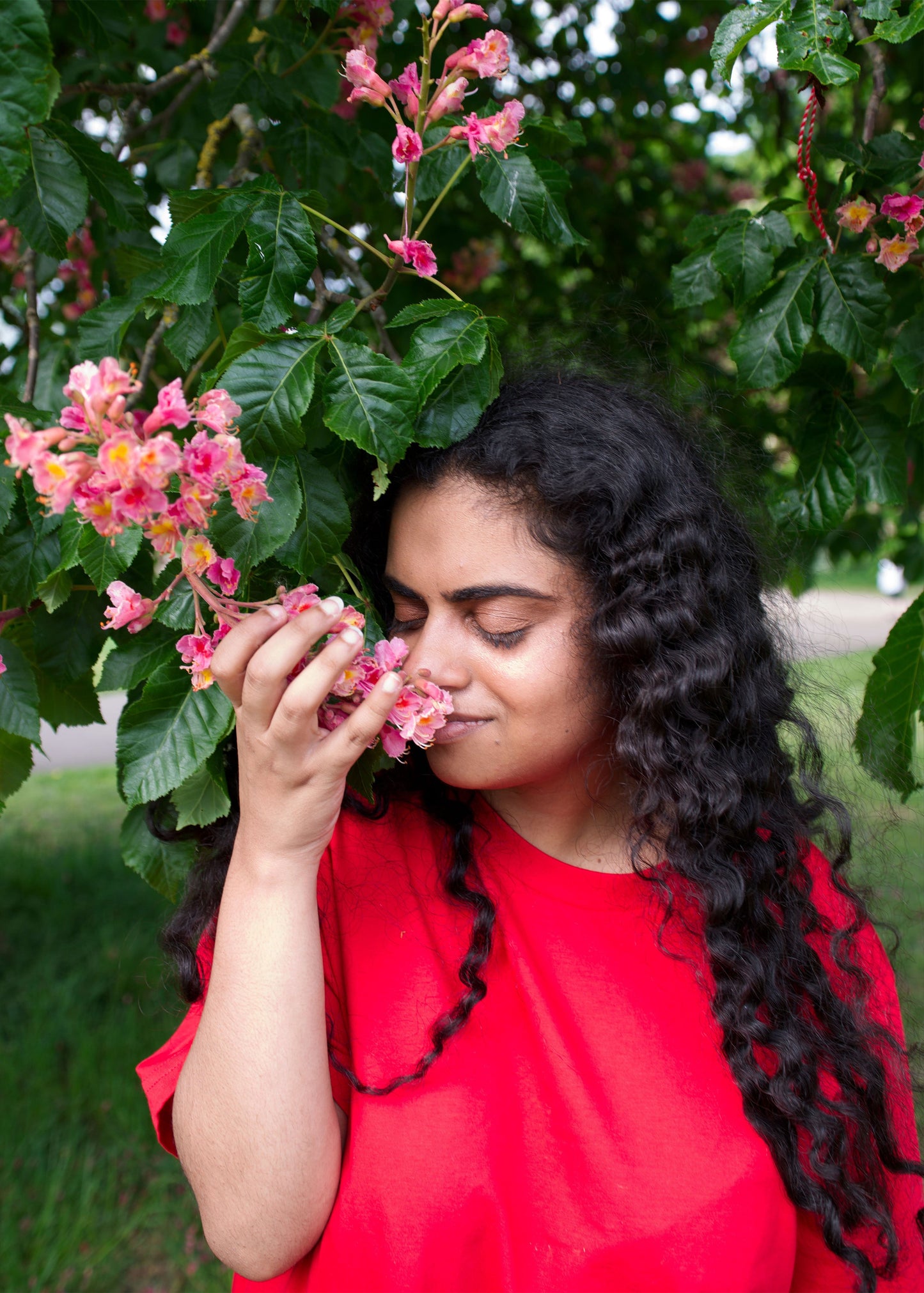 Woman in a red shirt smelling pink flowers in a garden