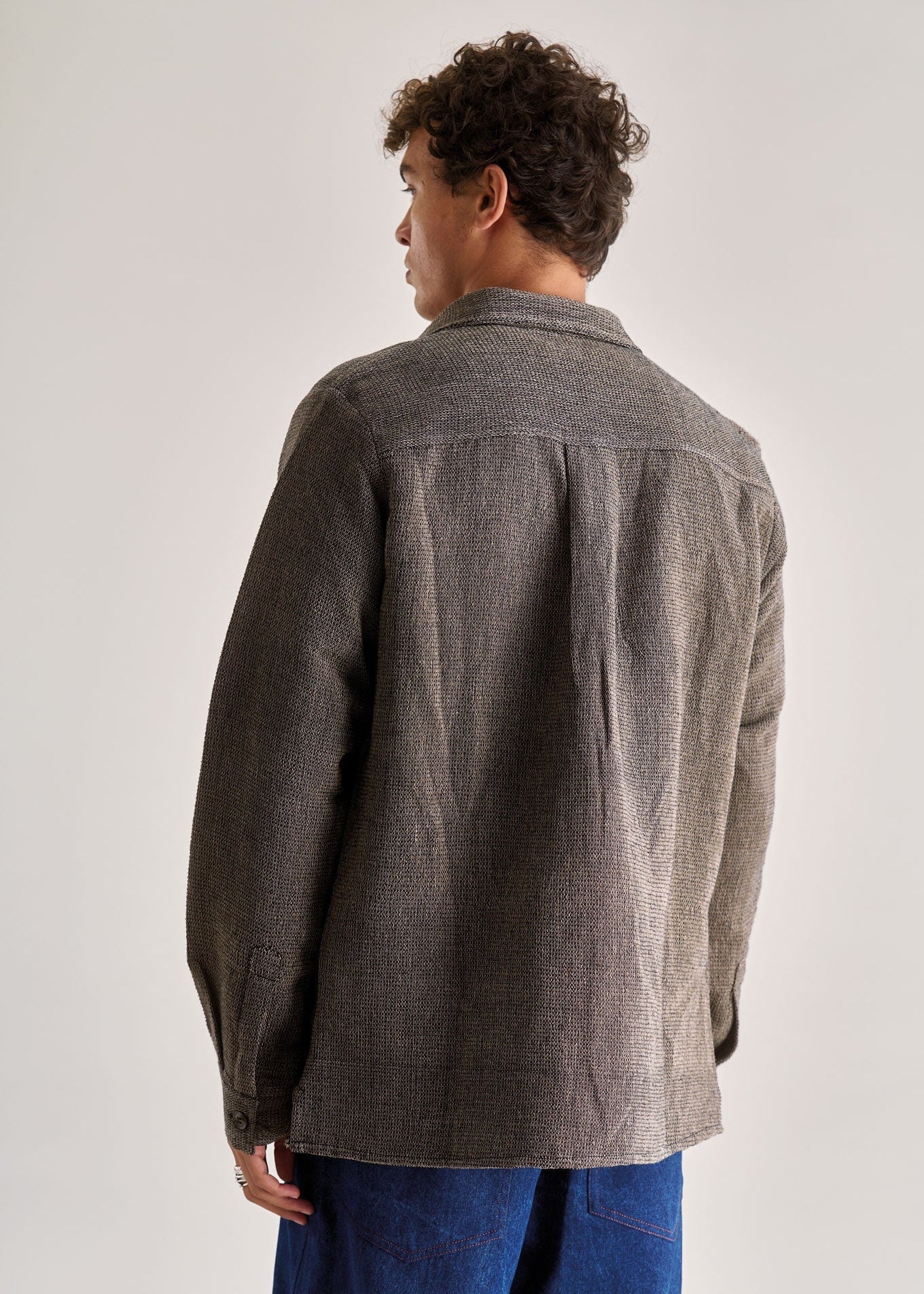 Person wearing a gray jacket and blue jeans on a white background
