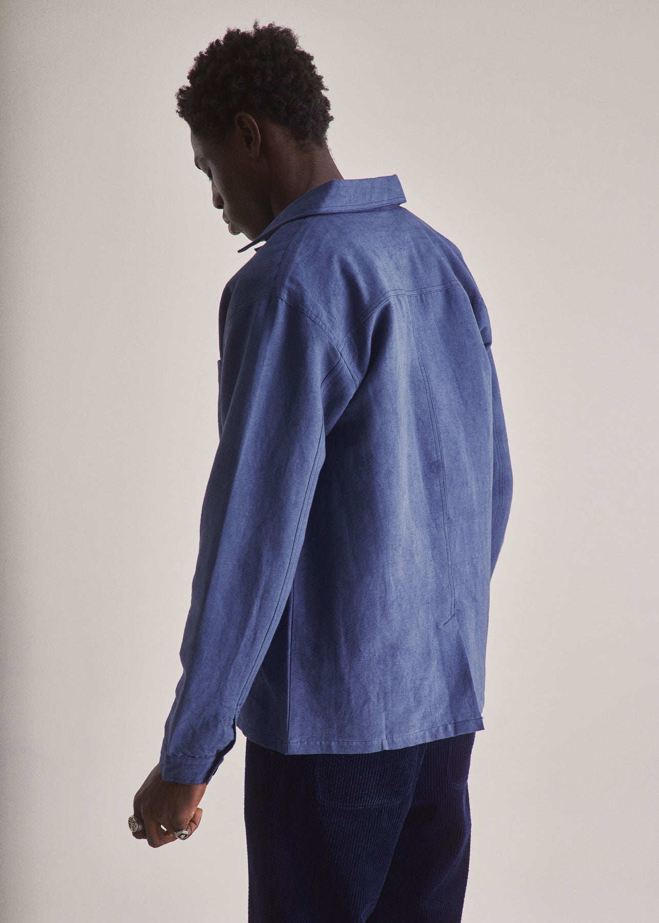 Person wearing a blue denim shirt and dark pants against a plain background