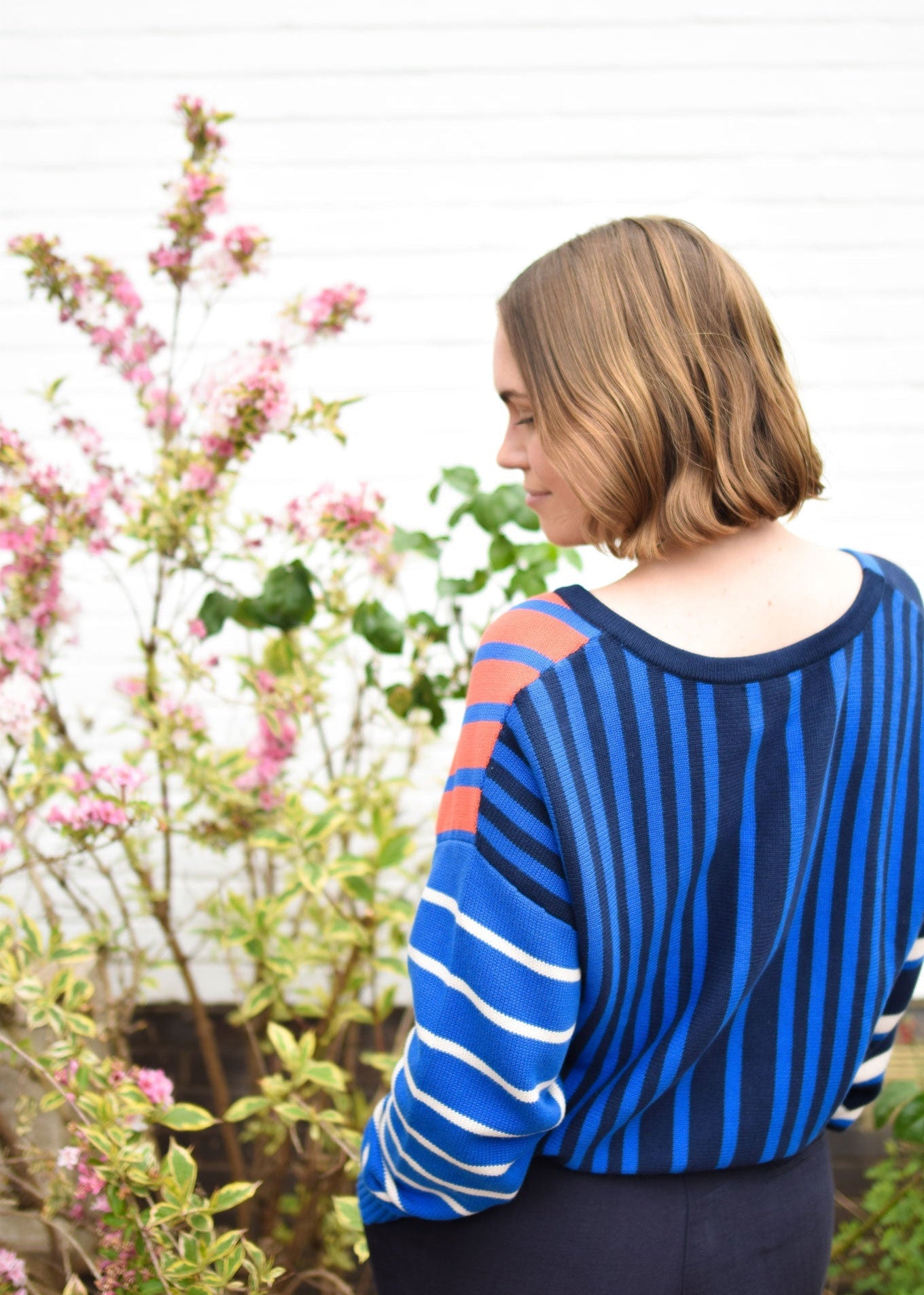 Person wearing a blue and orange striped sweater standing in a garden with pink flowers.